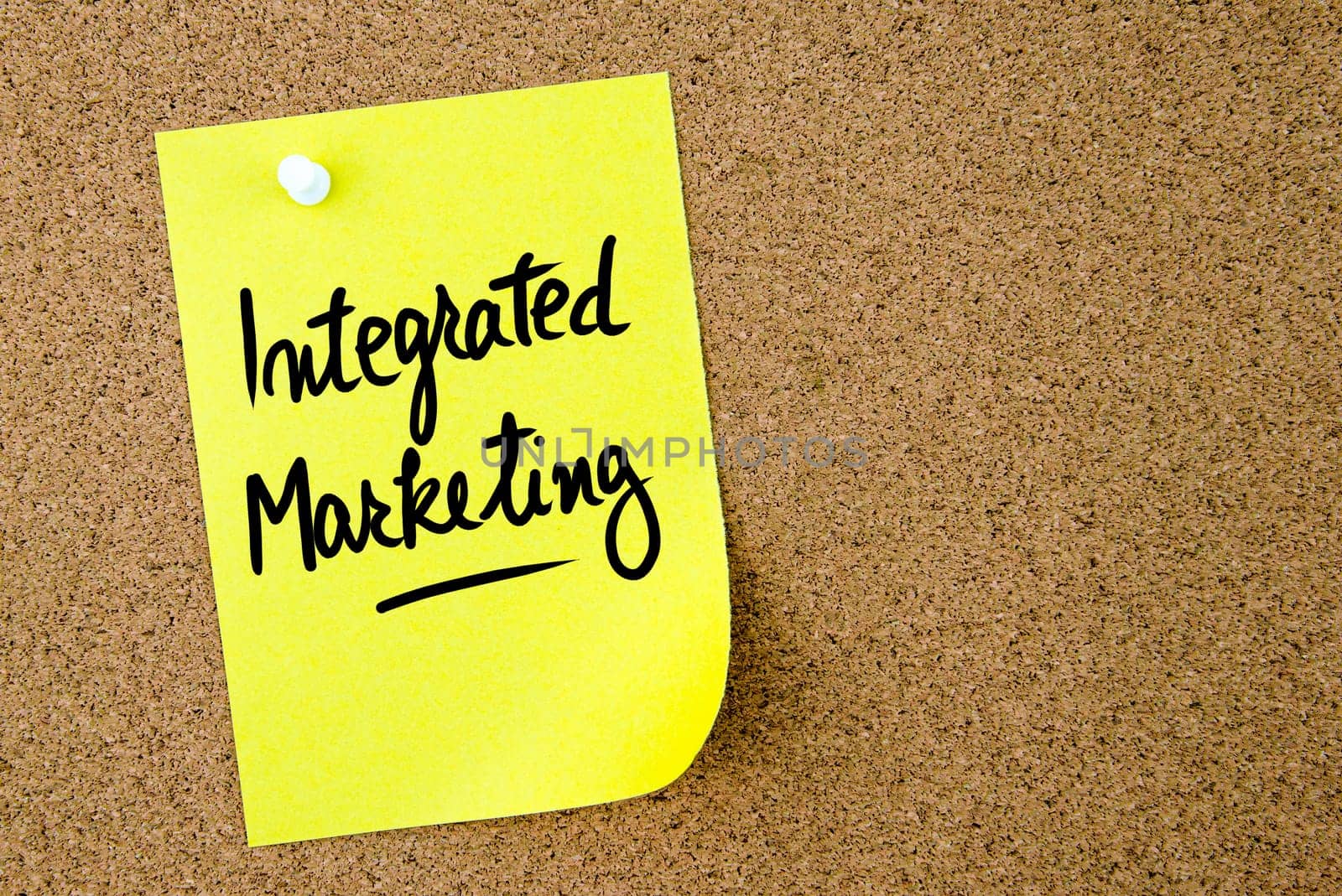 Integrated Marketing text written on yellow paper note pinned on cork board with white thumbtack. Business concept image with copy space available