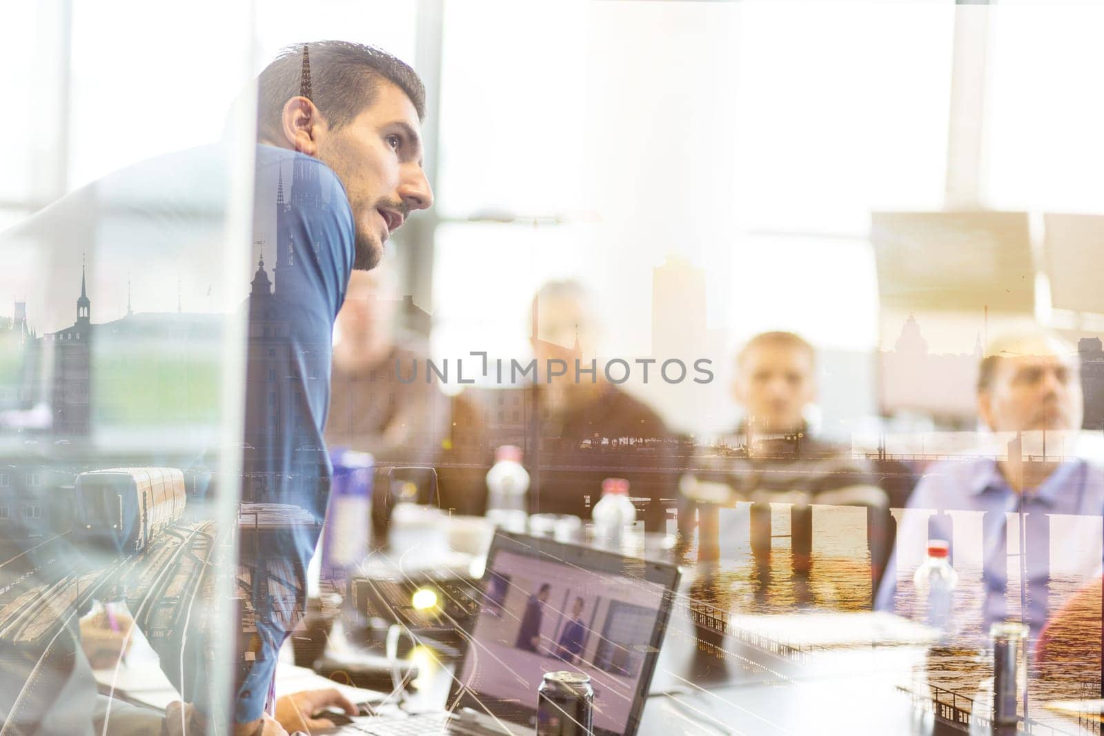 Business man making a presentation at office. Business executive delivering a presentation to his colleagues during meeting, explaining business plans to his employees. City reflection in window.