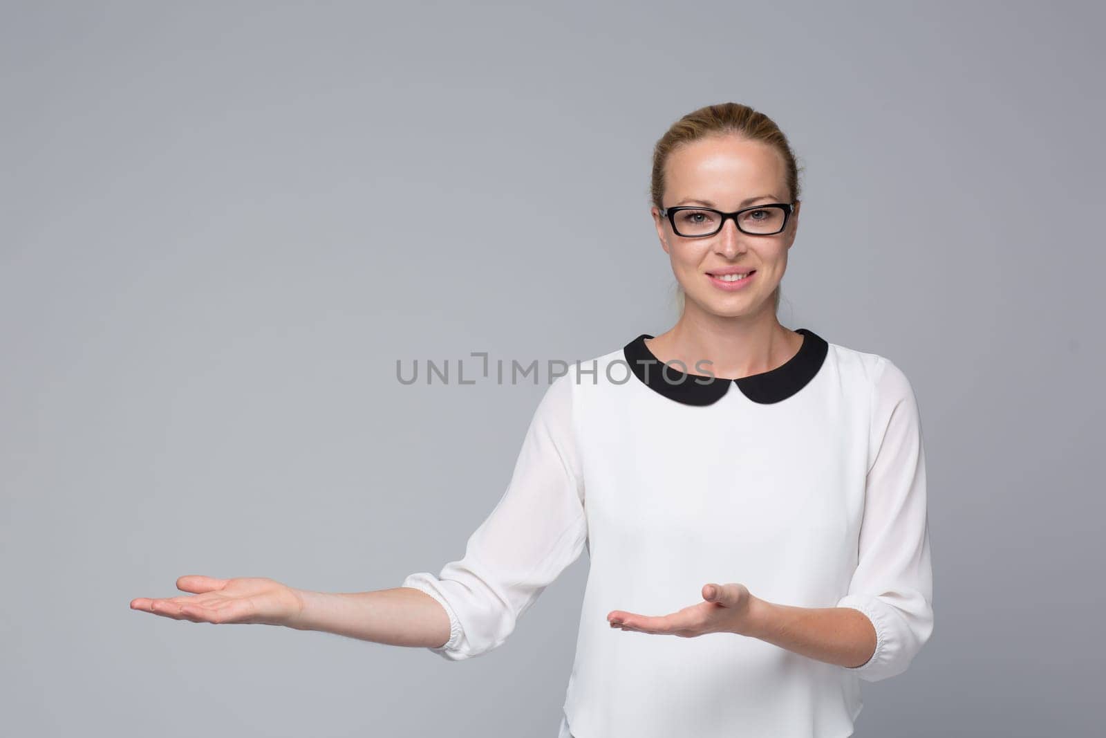 Beautiful young businesswoman smiling, holding open palm with empty copy space. Business woman showing hand sign to side, concept of advertisement product. Grey background.