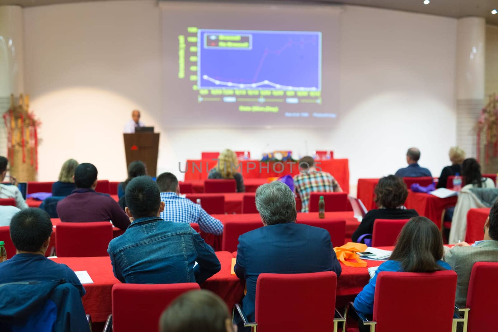 Speaker Giving a Talk at Business Meeting. Audience in the conference hall. Business and Entrepreneurship. Focus on unrecognizable people from rear.