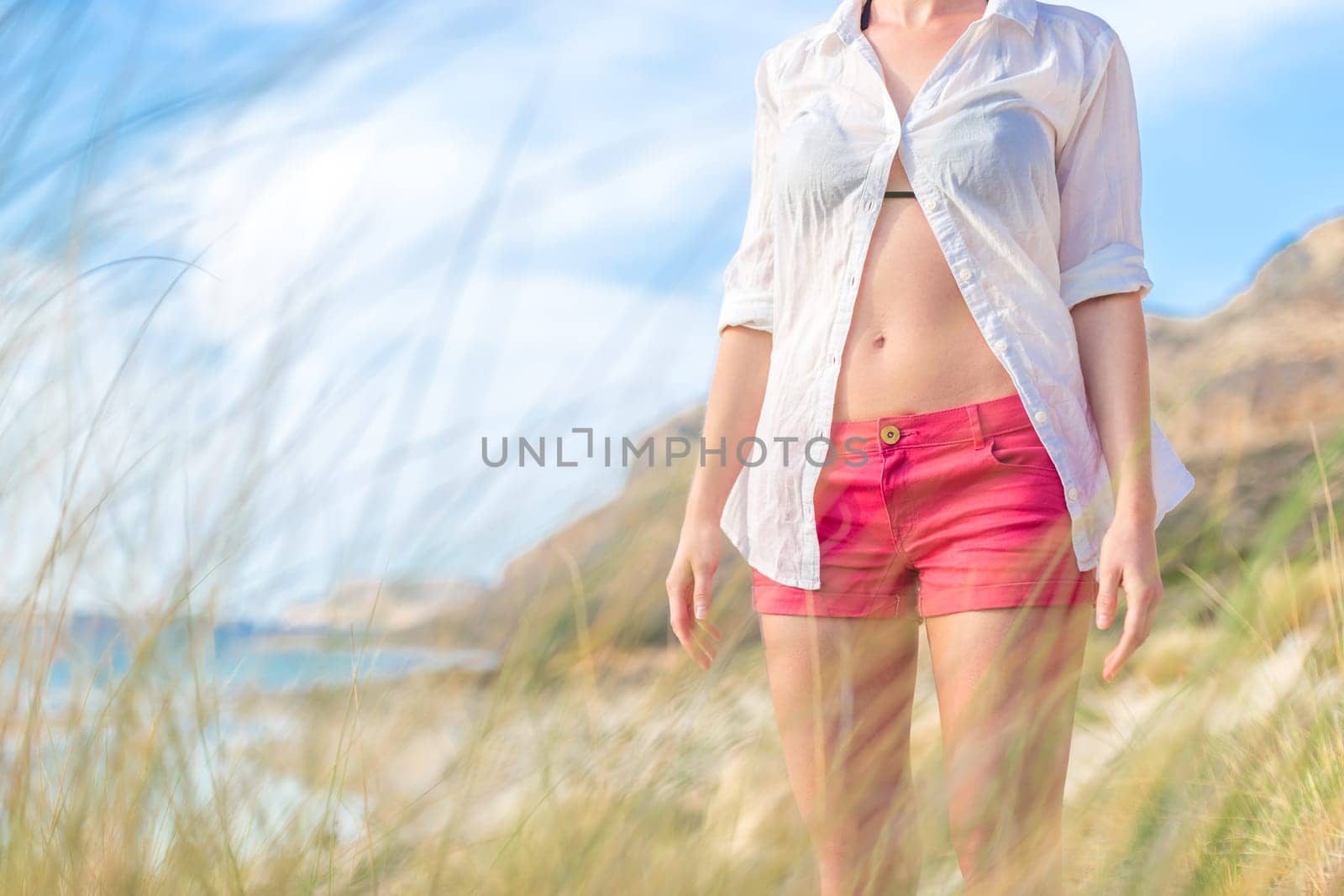 Relaxed woman in unpinned white shirt enjoying beautiful nature at serene landscape at Balos beach, Greece. Concept of vacations, freedom, happiness, joy and well being.