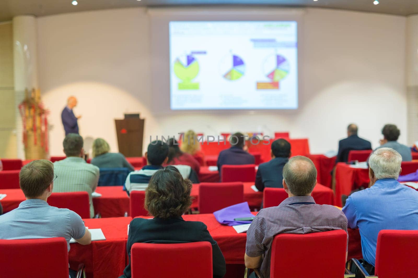 Speaker Giving a Talk at Business Meeting. Audience in the conference hall. Business and Entrepreneurship. Focus on unrecognizable people from rear.