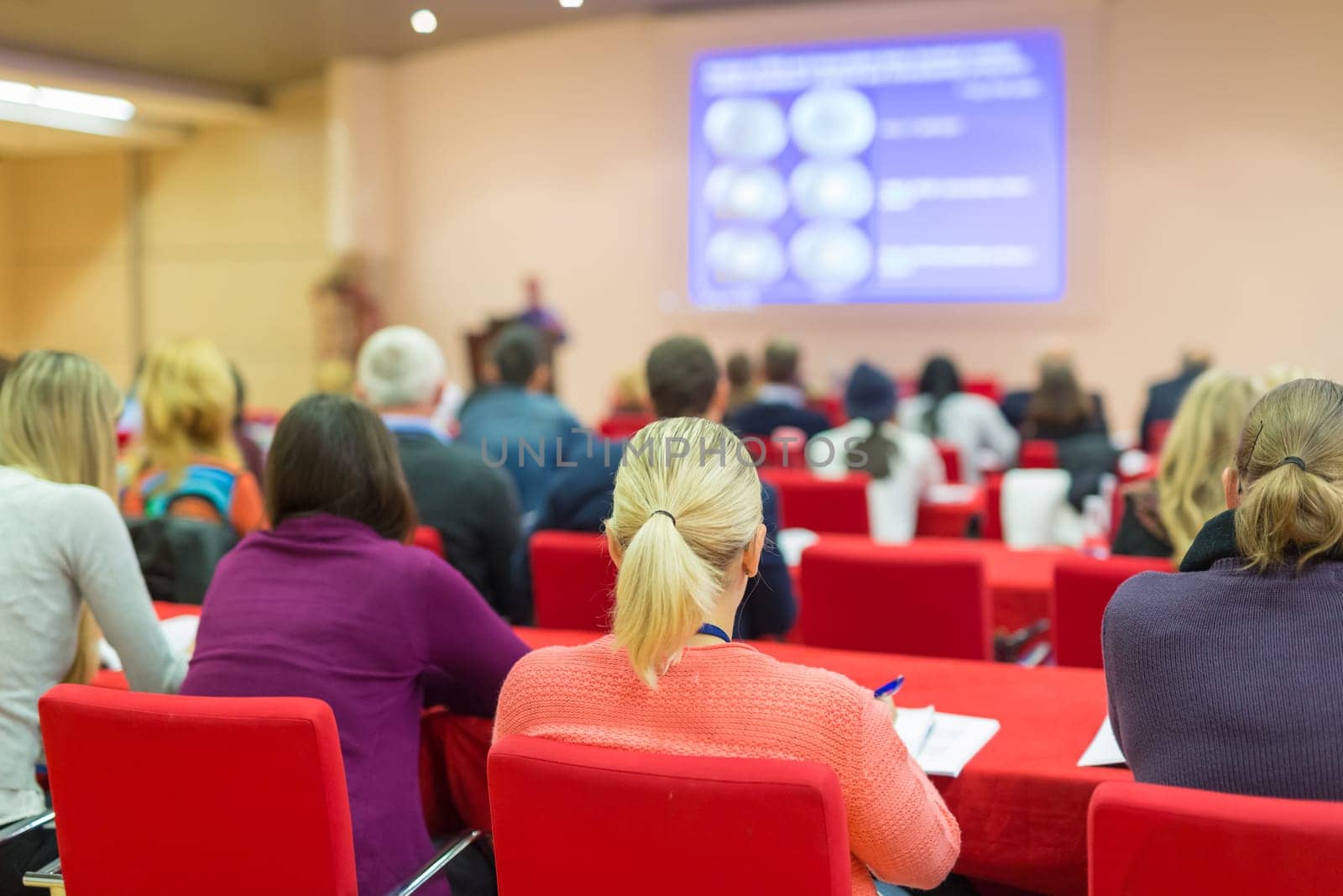 Speaker Giving a Talk at Business Meeting. Audience in the conference hall. Business and Entrepreneurship. Focus on unrecognizable people from rear.