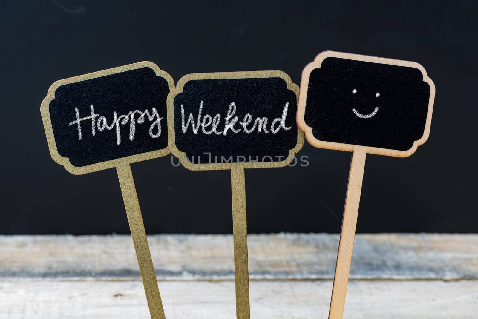 Motivational message Happy Weekend written with chalk on wooden mini blackboard labels, defocused chalkboard and wood table in background