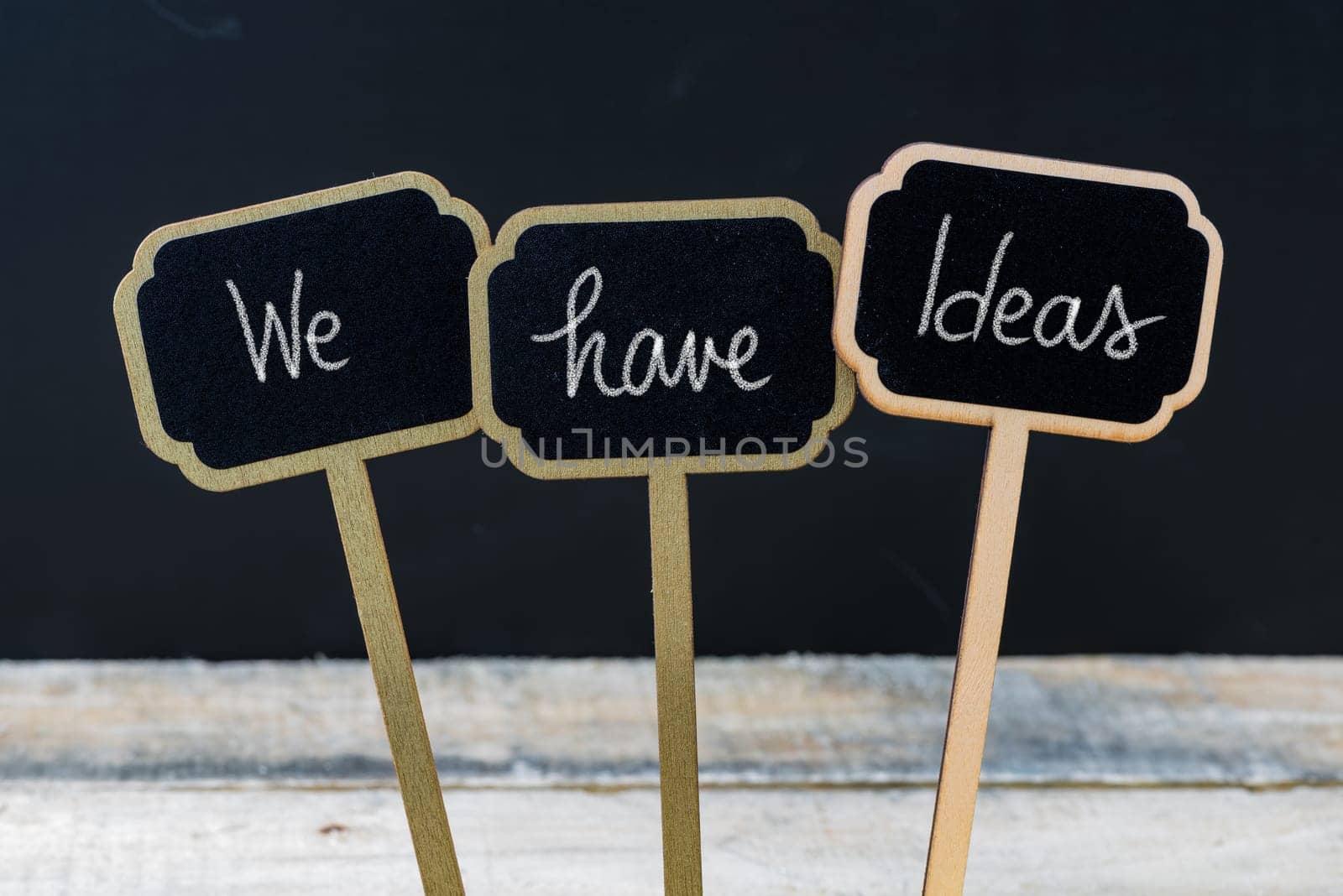 Motivational message We Have Ideas written with chalk on wooden mini blackboard labels, defocused chalkboard and wood table in background