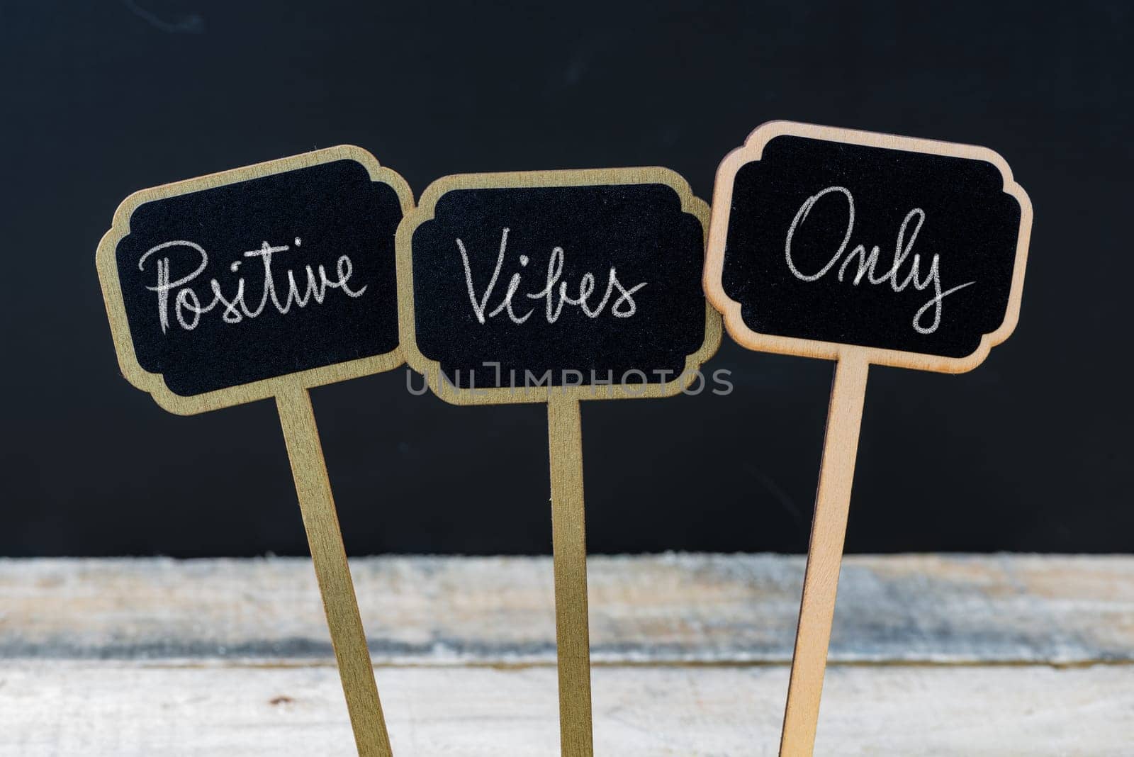 Motivational message Positive Vibes Only written with chalk on wooden mini blackboard labels, defocused chalkboard and wood table in background