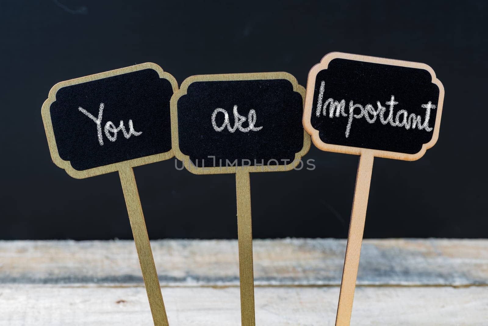 Motivational message YOU ARE IMPORTANT written with chalk on wooden mini blackboard labels, defocused chalkboard and wood table in background