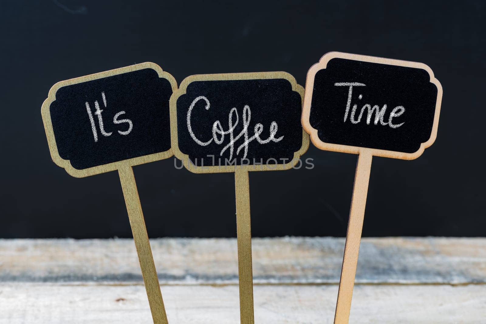 Motivational message Its Coffee Time written with chalk on wooden mini blackboard labels, defocused chalkboard and wood table in background