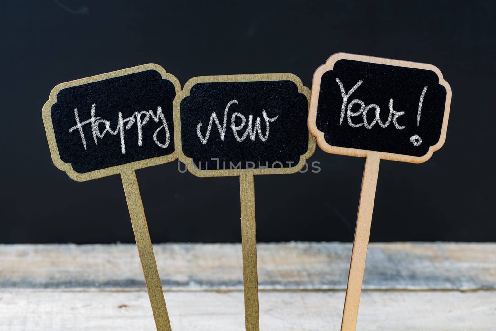 Motivational message Happy New Year written with chalk on wooden mini blackboard labels, defocused chalkboard and wood table in background