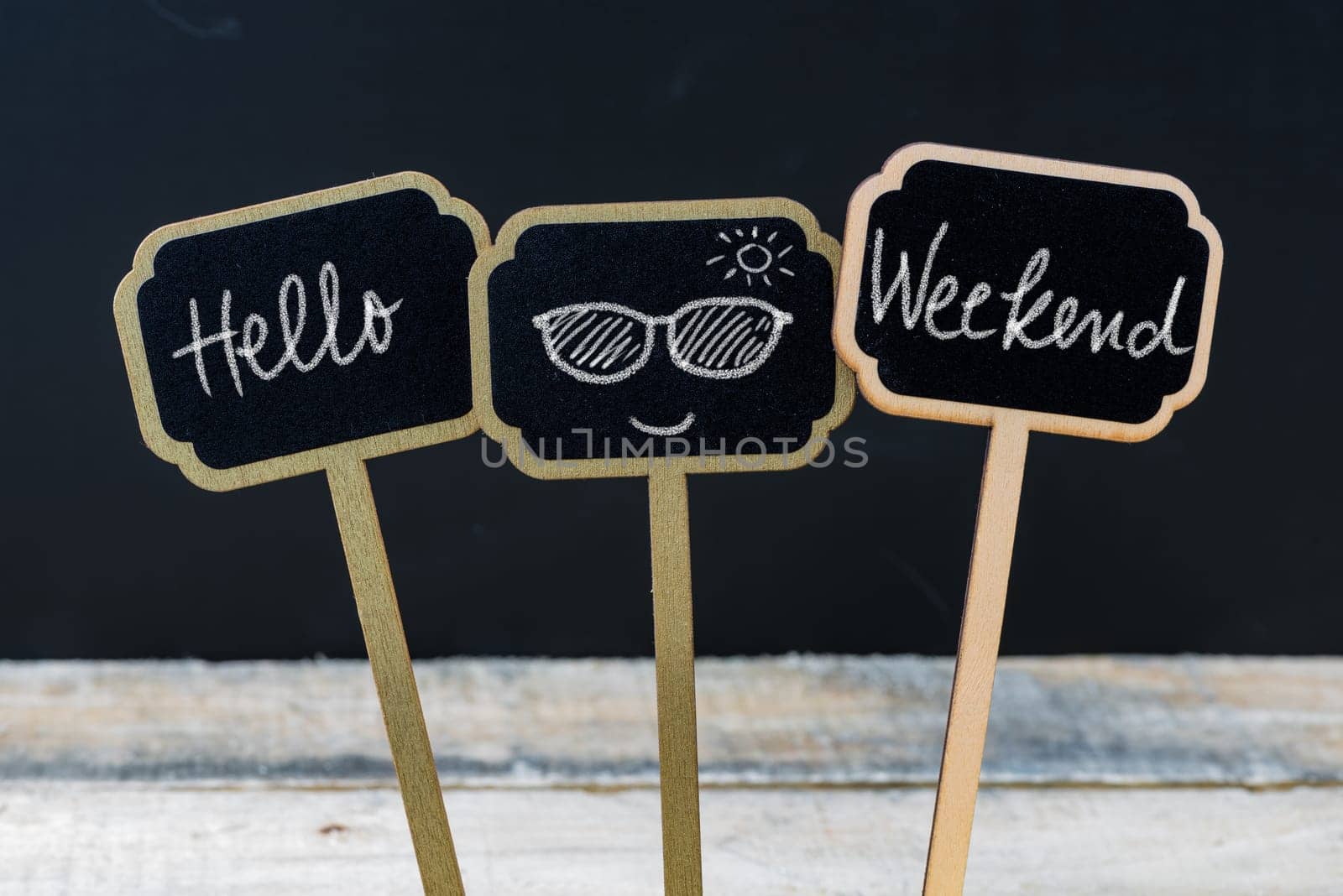 Motivational message Hello Weekend written with chalk on wooden mini blackboard labels, defocused chalkboard and wood table in background
