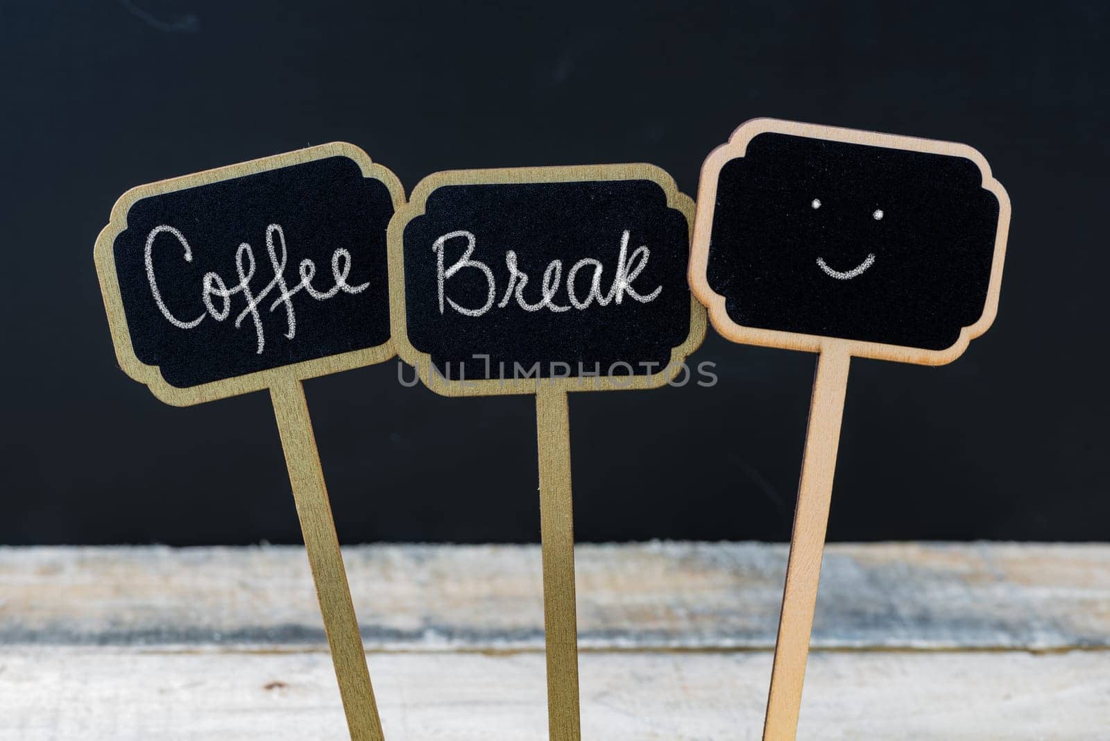 Motivational message Coffee Break written with chalk on wooden mini blackboard labels, defocused chalkboard and wood table in background