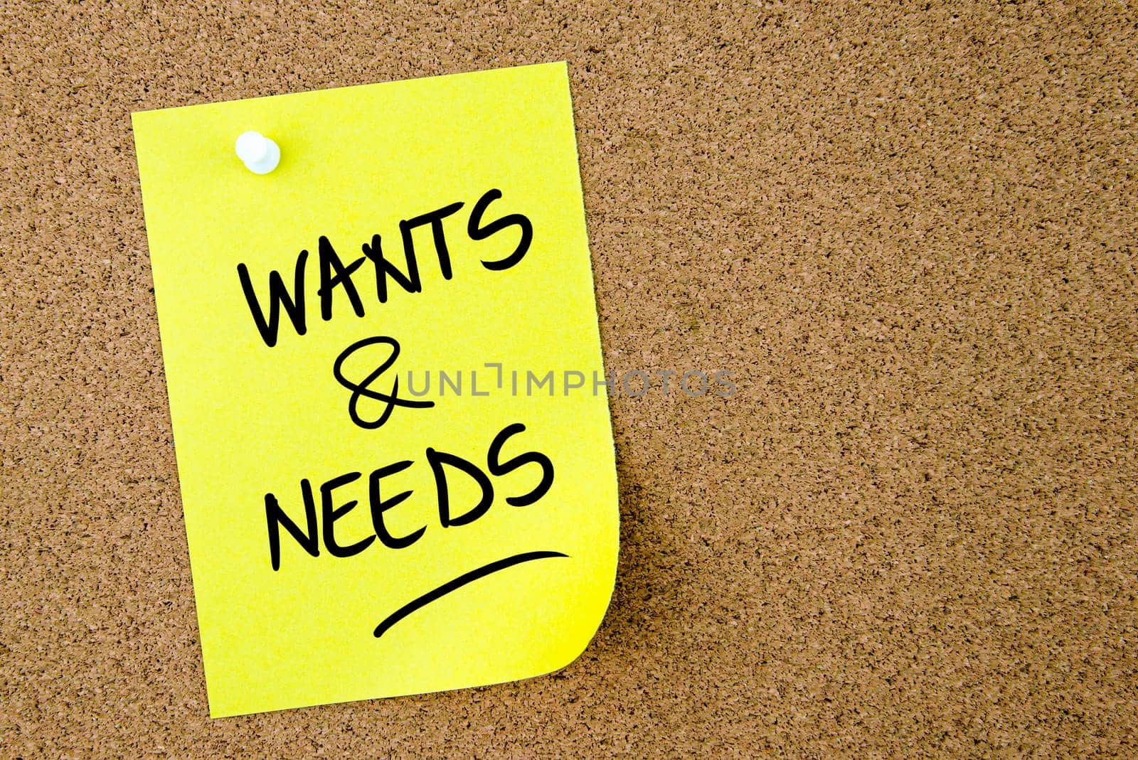 Wants and Needs text written on yellow paper note pinned on cork board with white thumbtack. Business concept image with copy space available