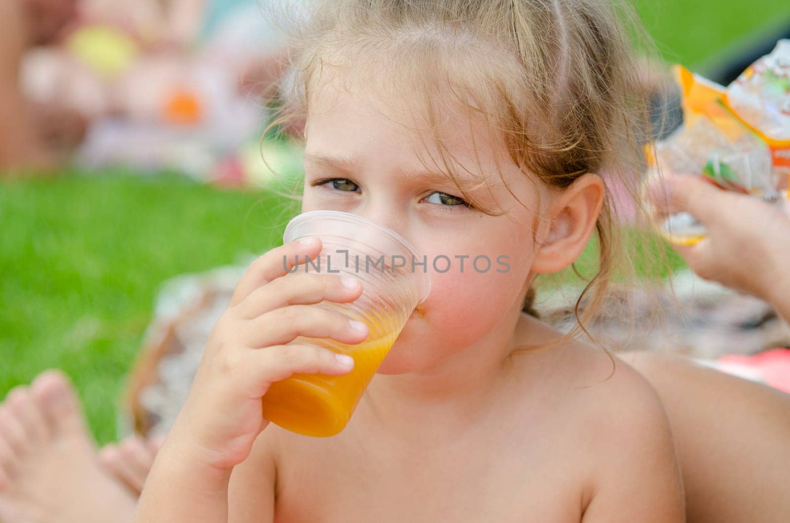 Girl drinking fruit juice from a plastic disposable cup and looked into the frame