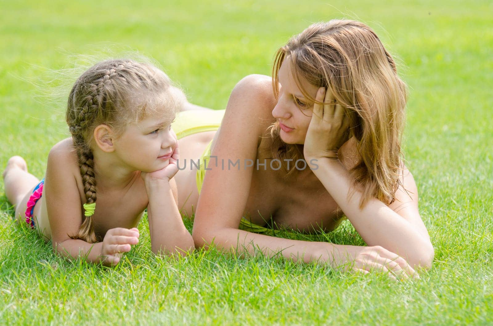 Young mother and five year old daughter lying on green grass and looking at each other