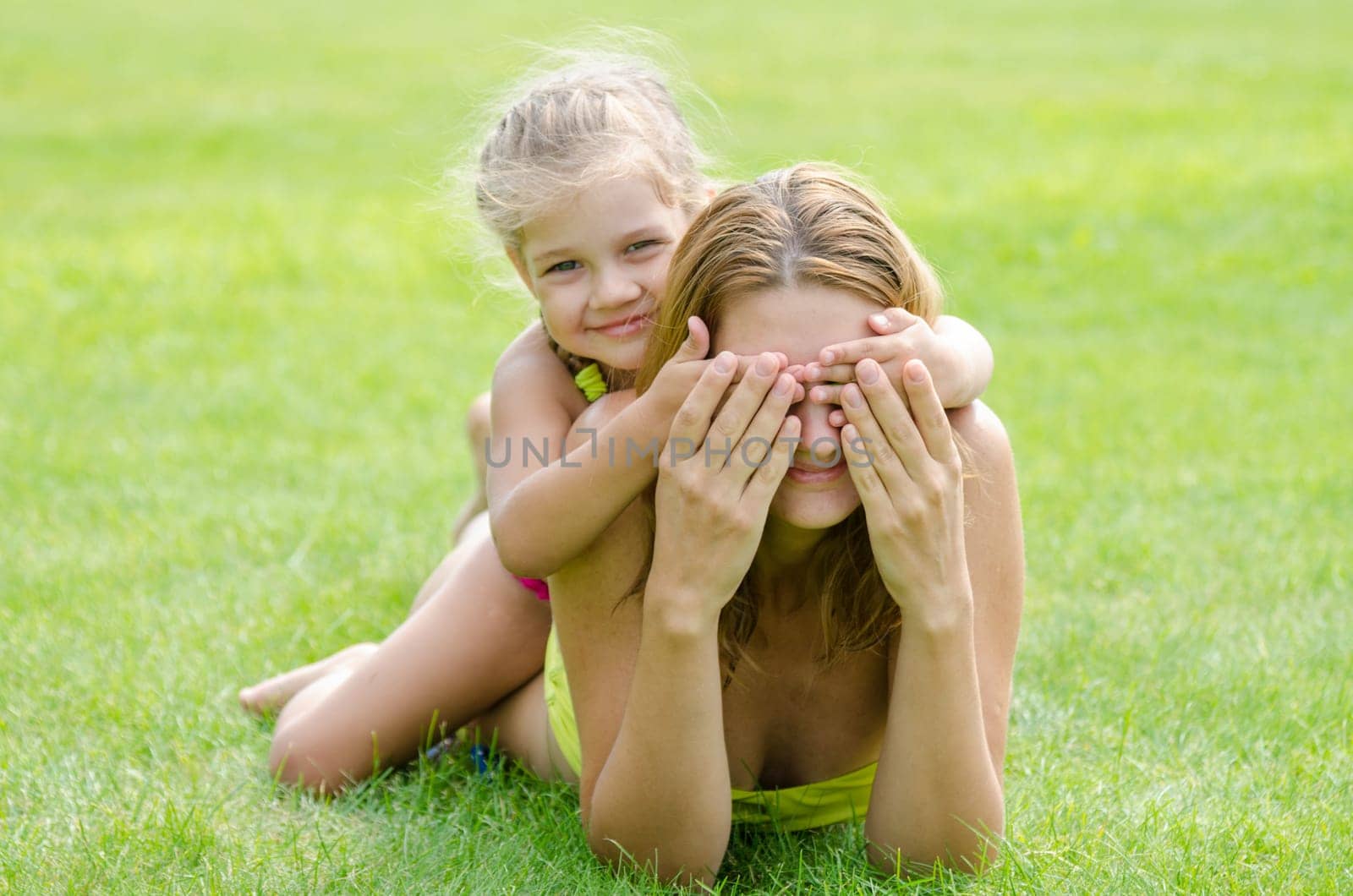 The daughter of fun mom closed her eyes while lying on a green lawn