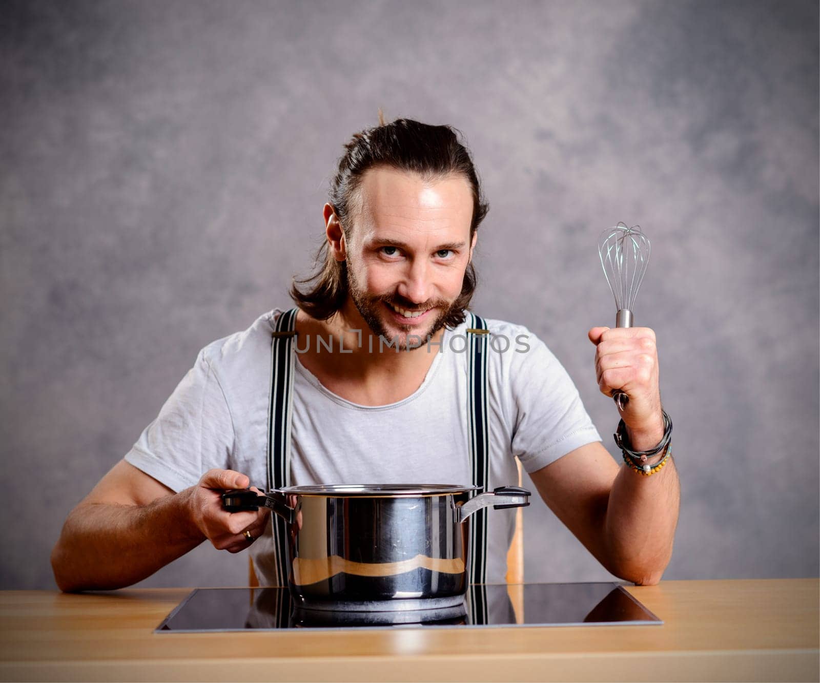 young bearded man with cooking pot and egg whish in front of gray background