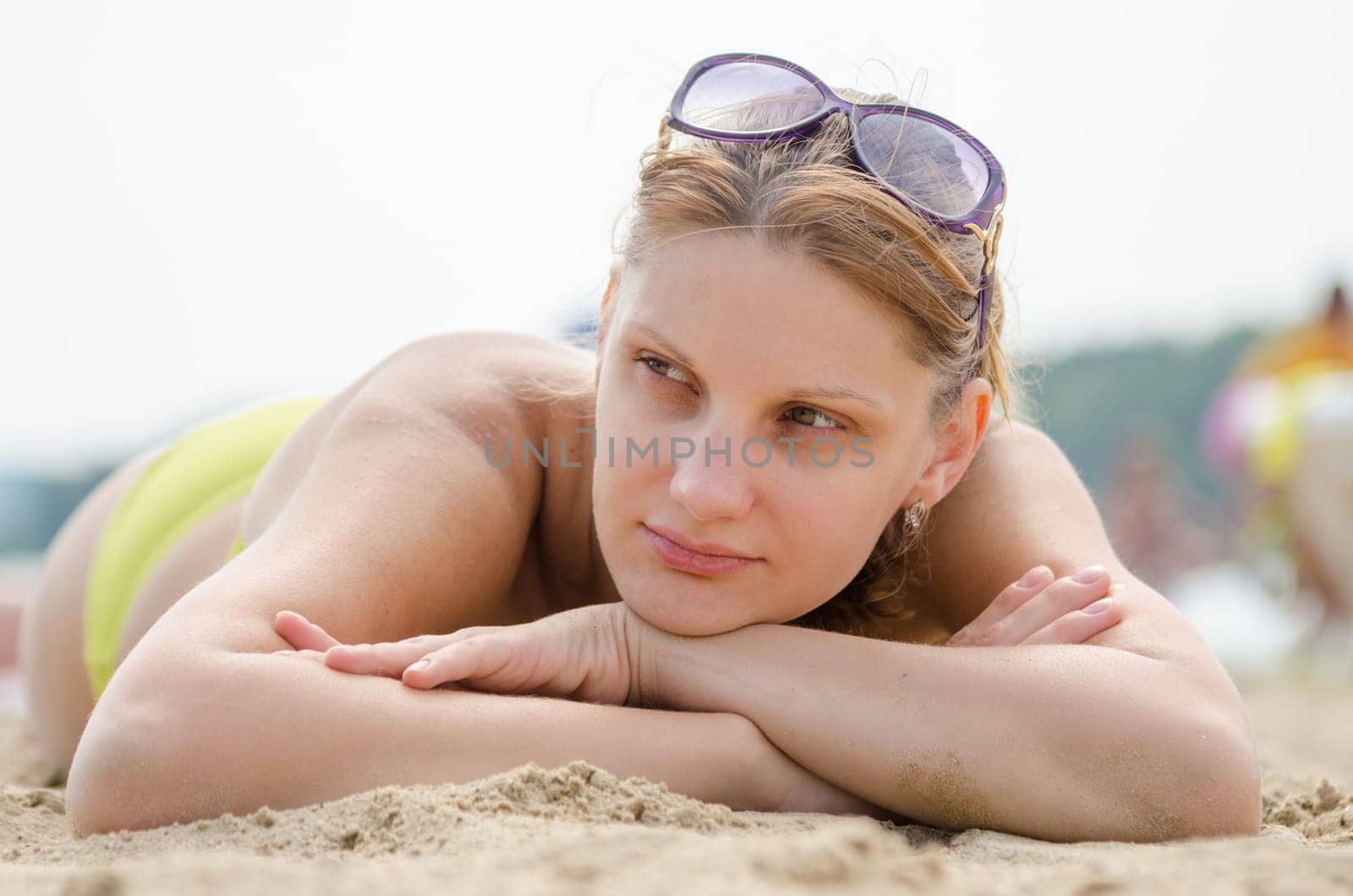 Sad young girl lying on sandy beach and looking to the side