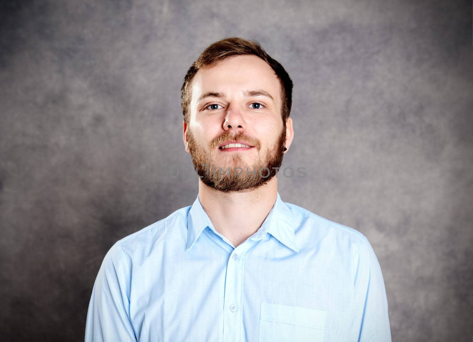 young bearded man in blue shirt in front of gray background