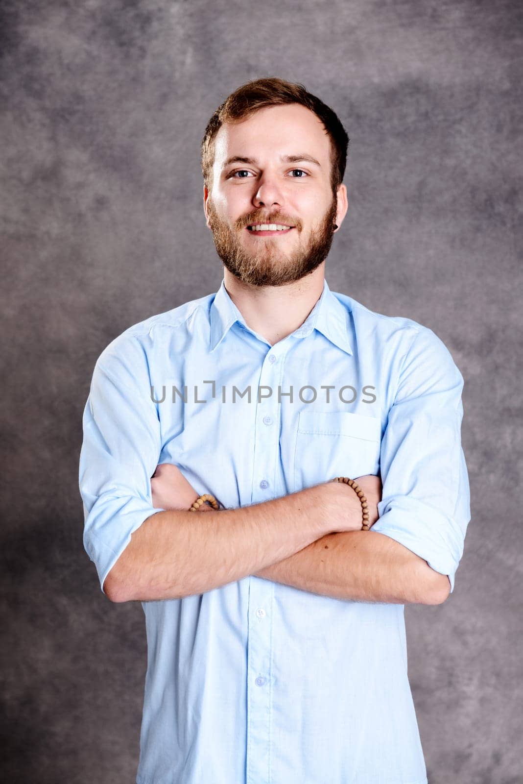 young bearded man with crossed arms in front of gray background