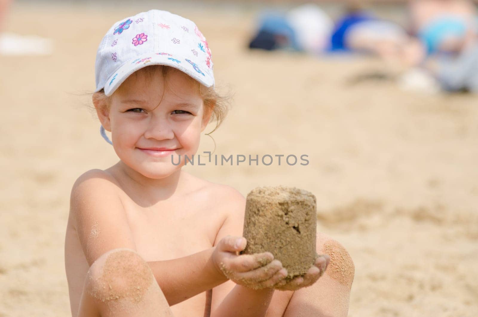 Girl keeps hands on the turret of sand sitting on a river beach
