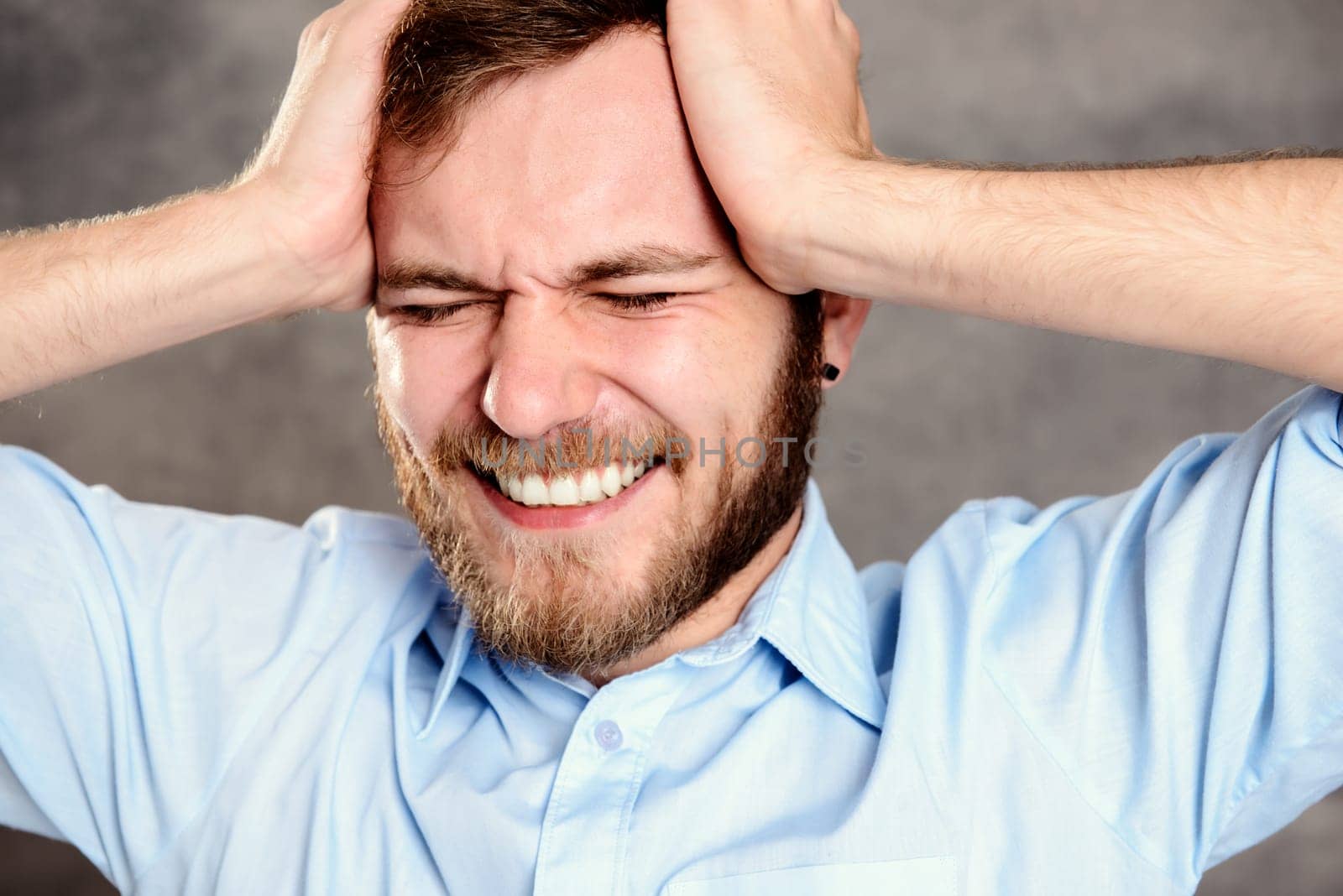 young bearded man in front of gray background has headache