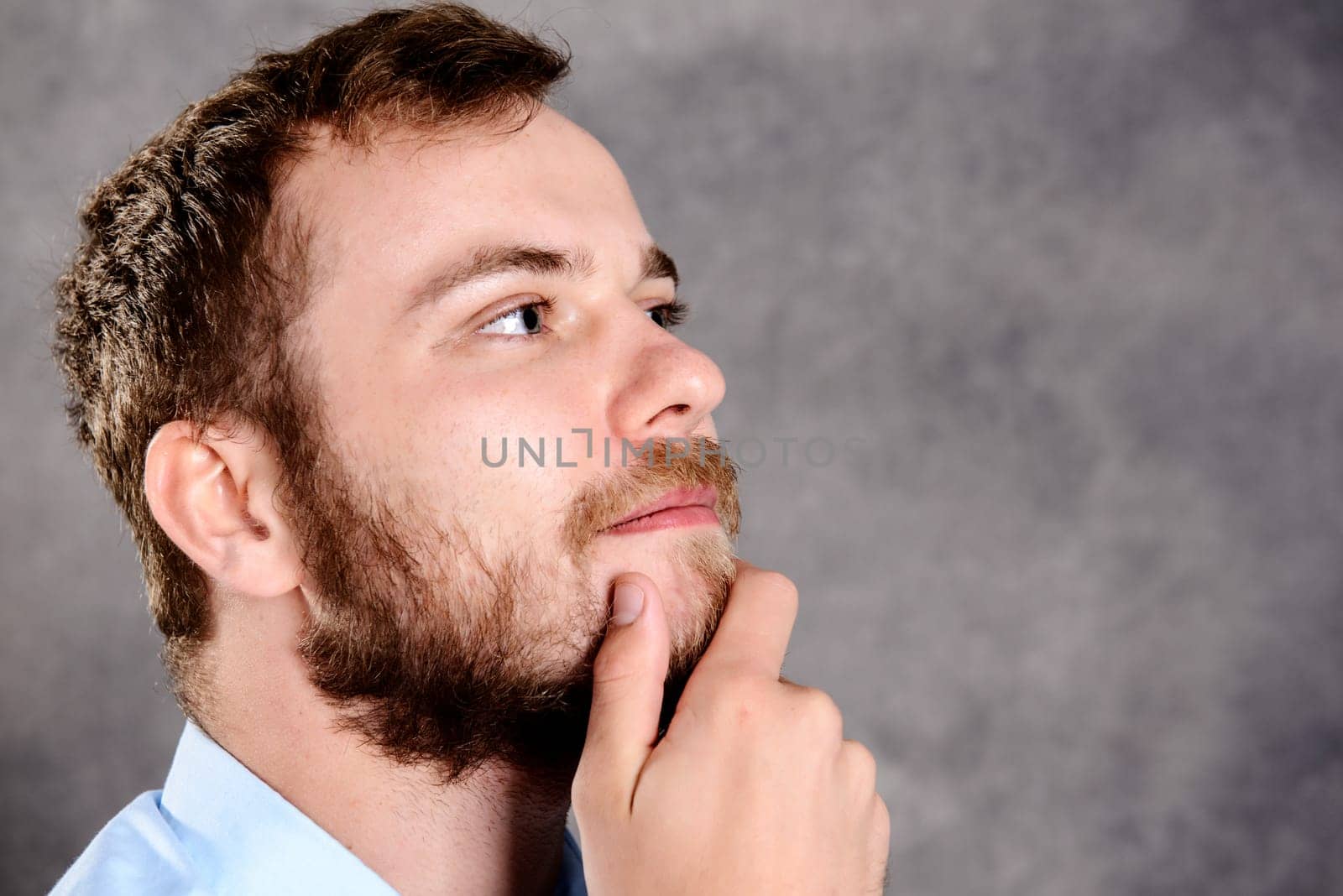 young bearded man in front of gray background is reflecting