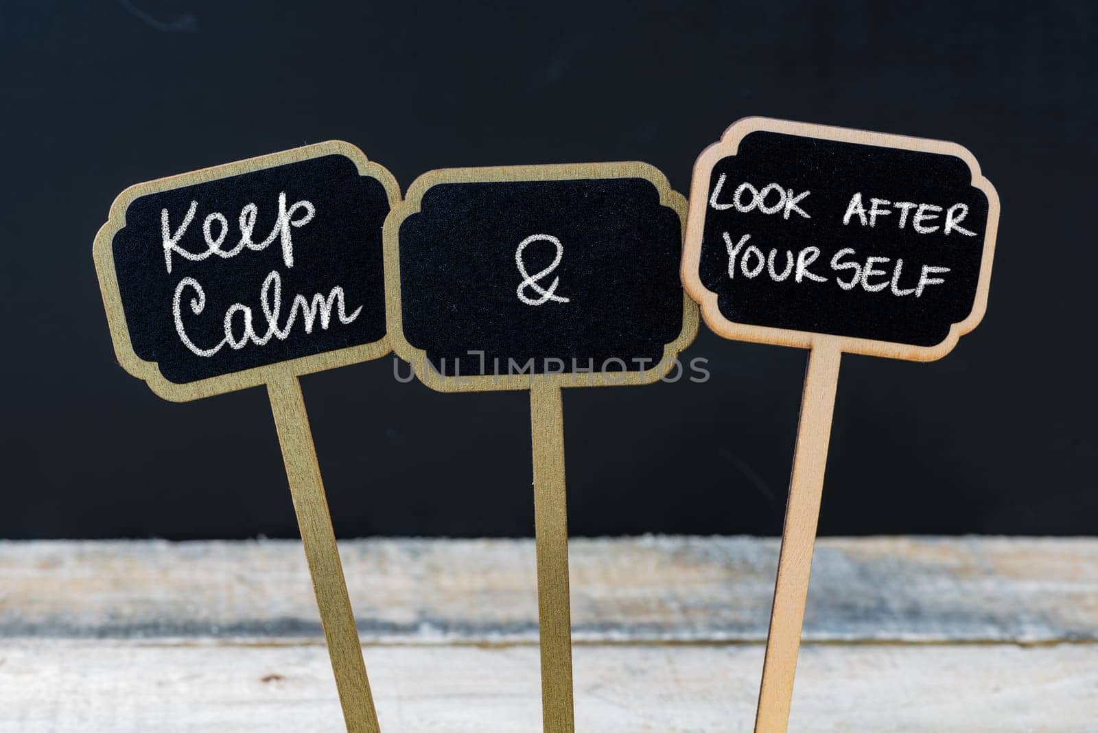 Keep Calm and Look After Yourself message written with chalk on mini blackboard labels, defocused chalkboard and wooden table in background. Fun and humor concept