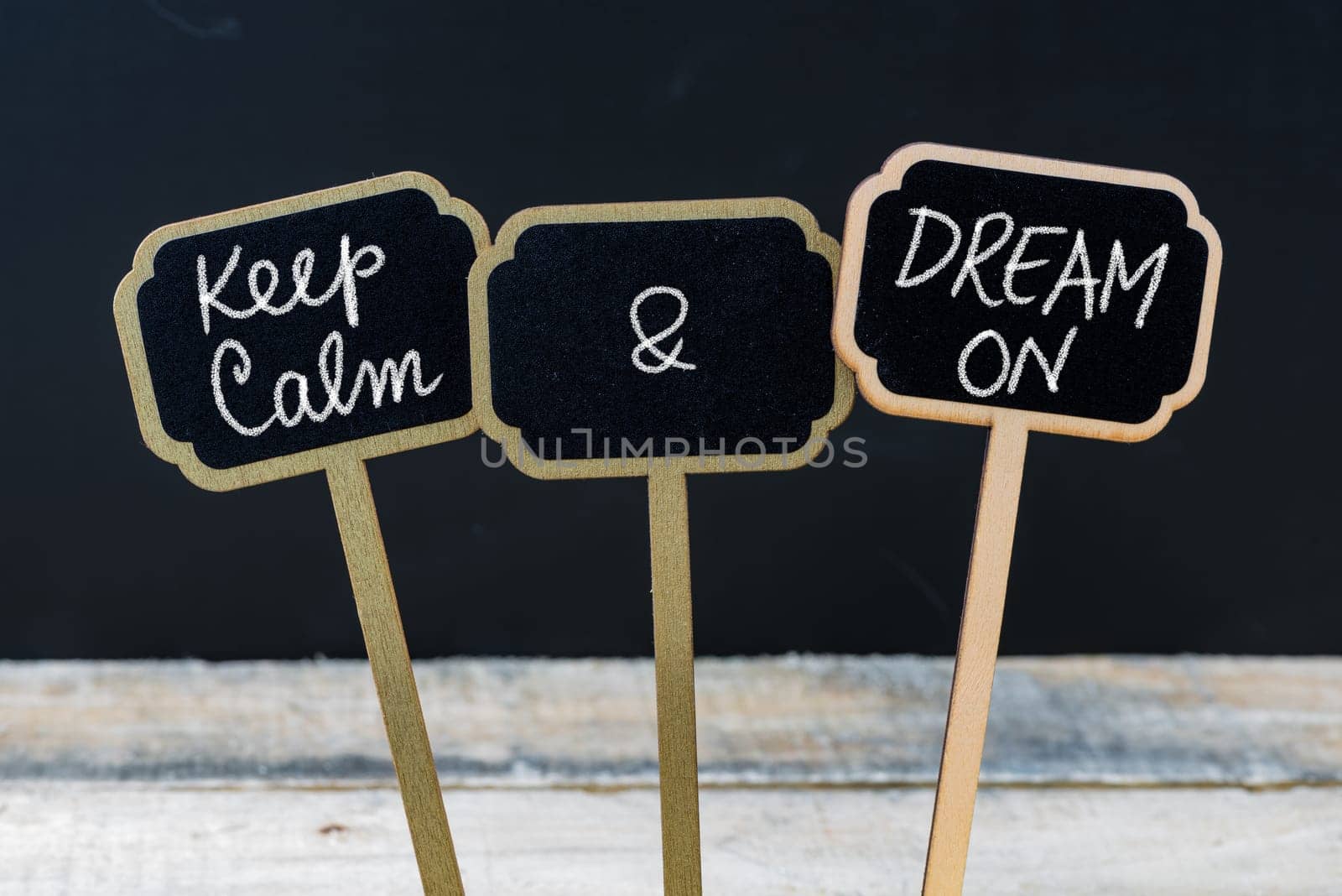 Keep Calm and Dream On message written with chalk on mini blackboard labels, defocused chalkboard and wooden table in background. Fun and humor concept