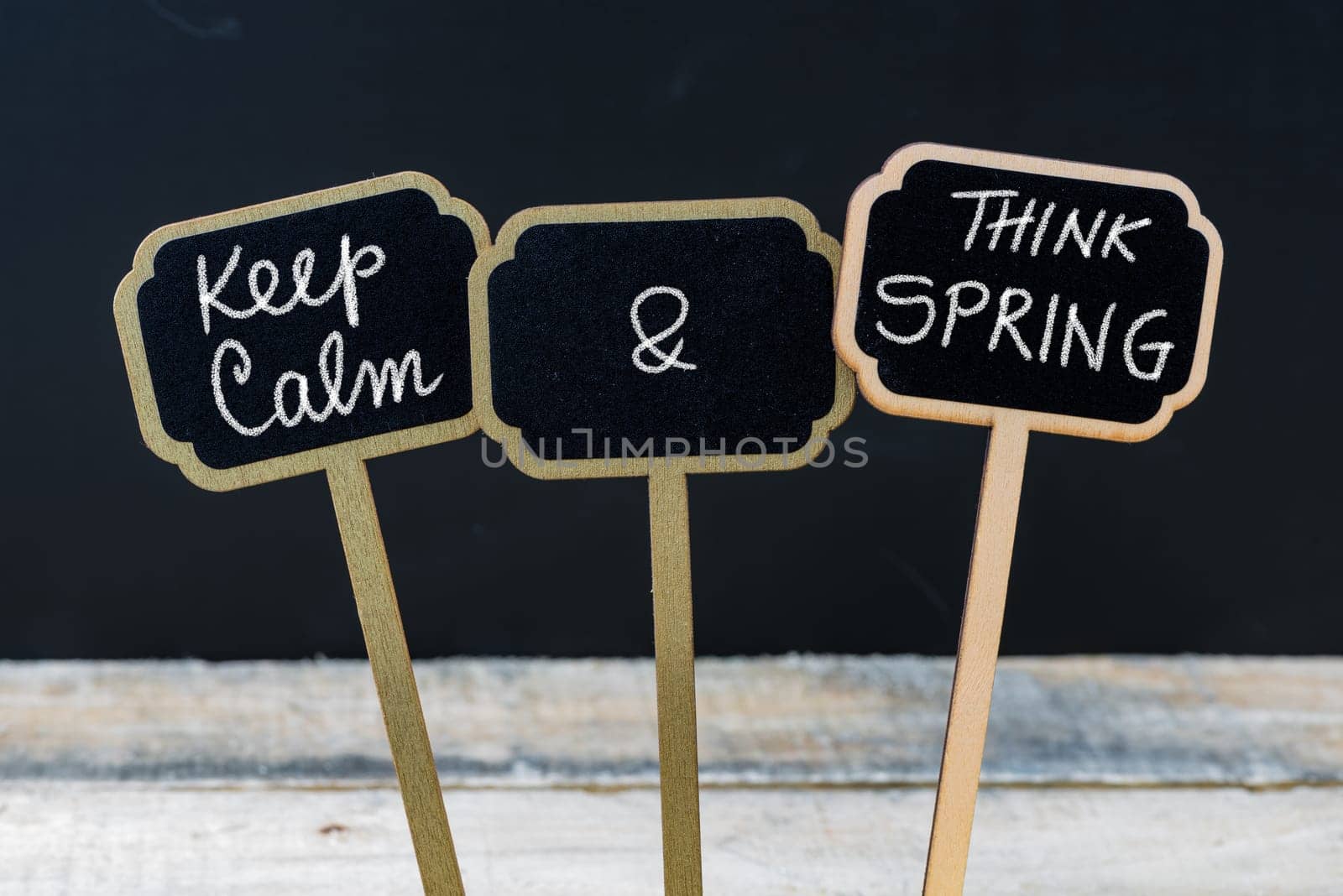 Keep Calm and Think Spring message written with chalk on mini blackboard labels, defocused chalkboard and wooden table in background. Fun and humor concept