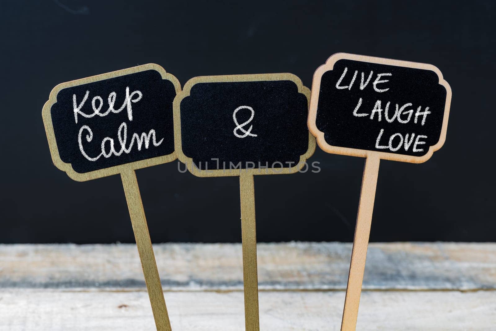 Keep Calm and Live Laugh Love message written with chalk on mini blackboard labels, defocused chalkboard and wooden table in background. Fun and humor concept