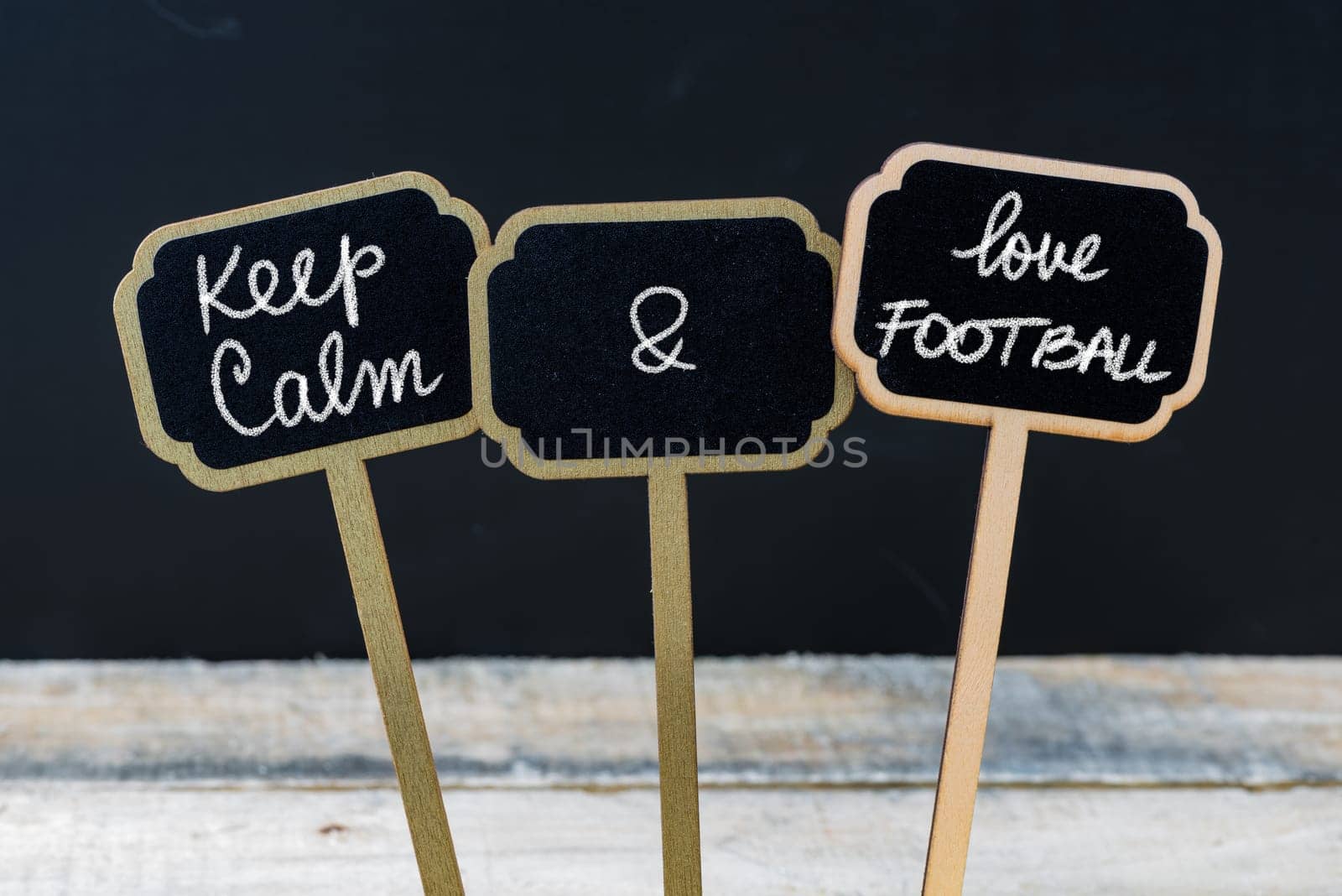 Keep Calm and Love Football message written with chalk on mini blackboard labels, defocused chalkboard and wooden table in background. Fun and humor concept