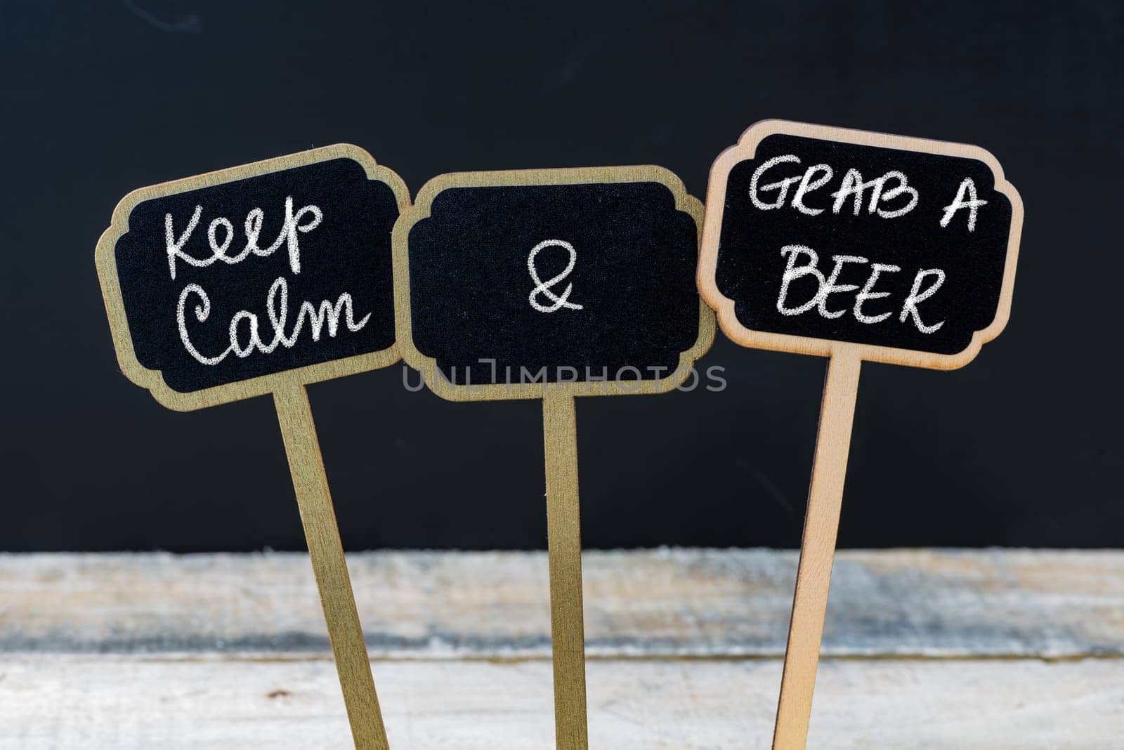 Keep Calm and Grab A Beer message written with chalk on mini blackboard labels, defocused chalkboard and wooden table in background. Fun and humor concept