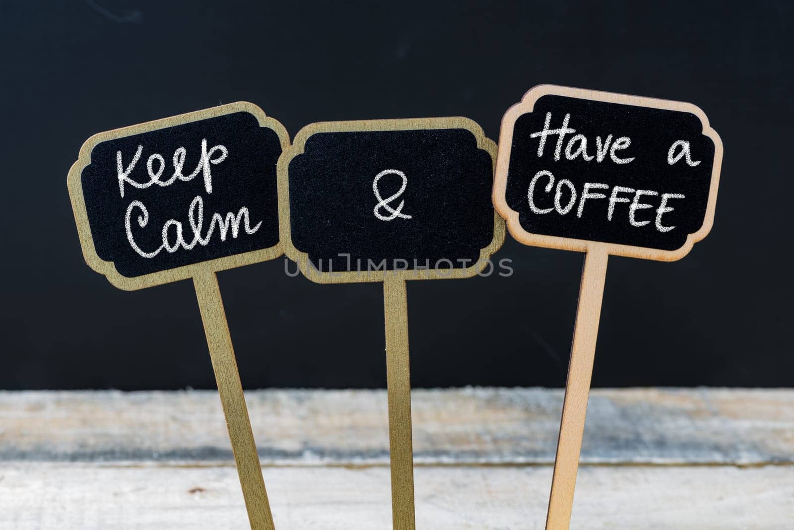 Keep Calm and Have A Coffee message written with chalk on mini blackboard labels, defocused chalkboard and wooden table in background. Fun and humor concept