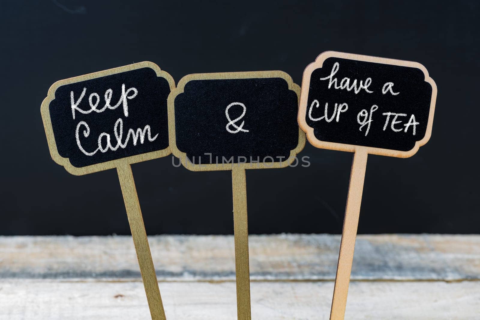 Keep Calm and Have A Cup Of Tea message written with chalk on mini blackboard labels, defocused chalkboard and wooden table in background. Fun and humor concept