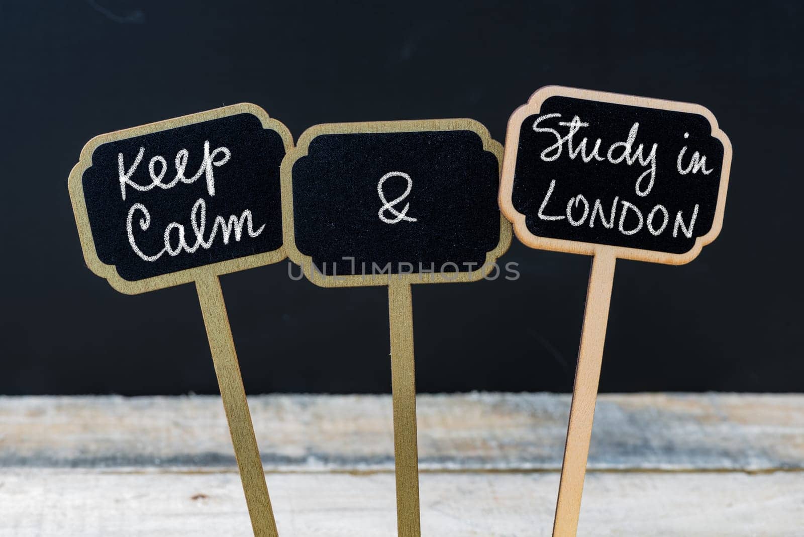 Keep Calm and Study In London message written with chalk on mini blackboard labels, defocused chalkboard and wooden table in background. Fun and humor concept