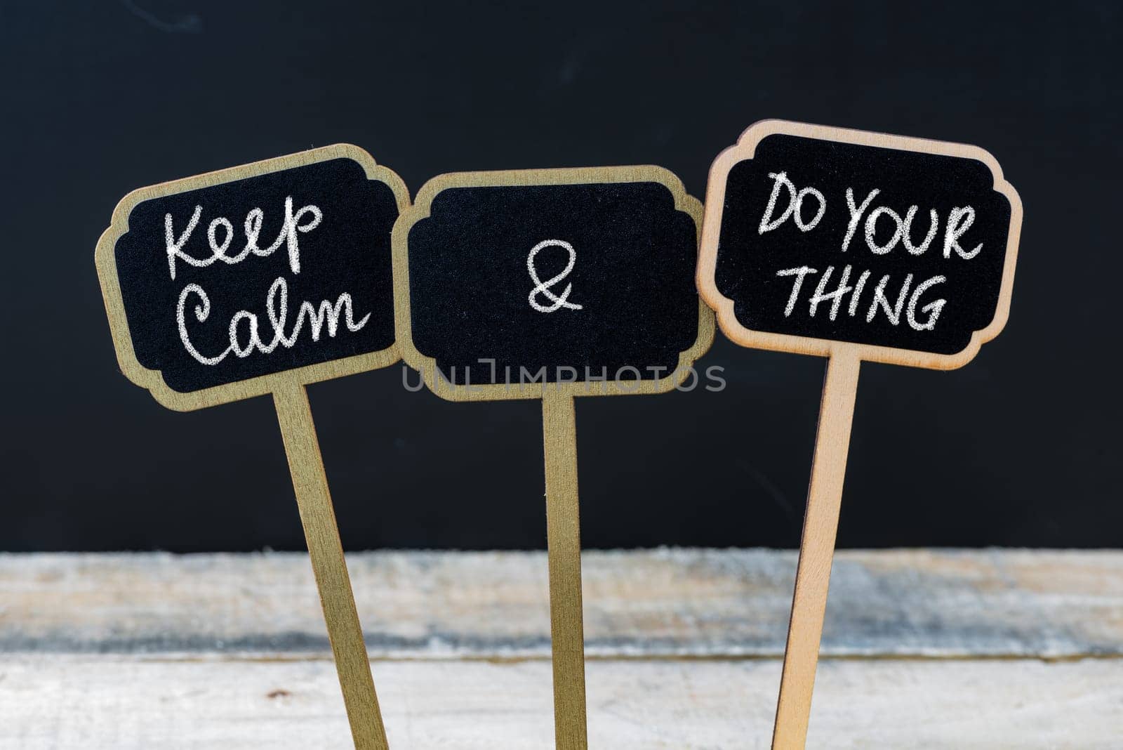 Keep Calm and Do Your Thing message written with chalk on mini blackboard labels, defocused chalkboard and wooden table in background. Fun and humor concept