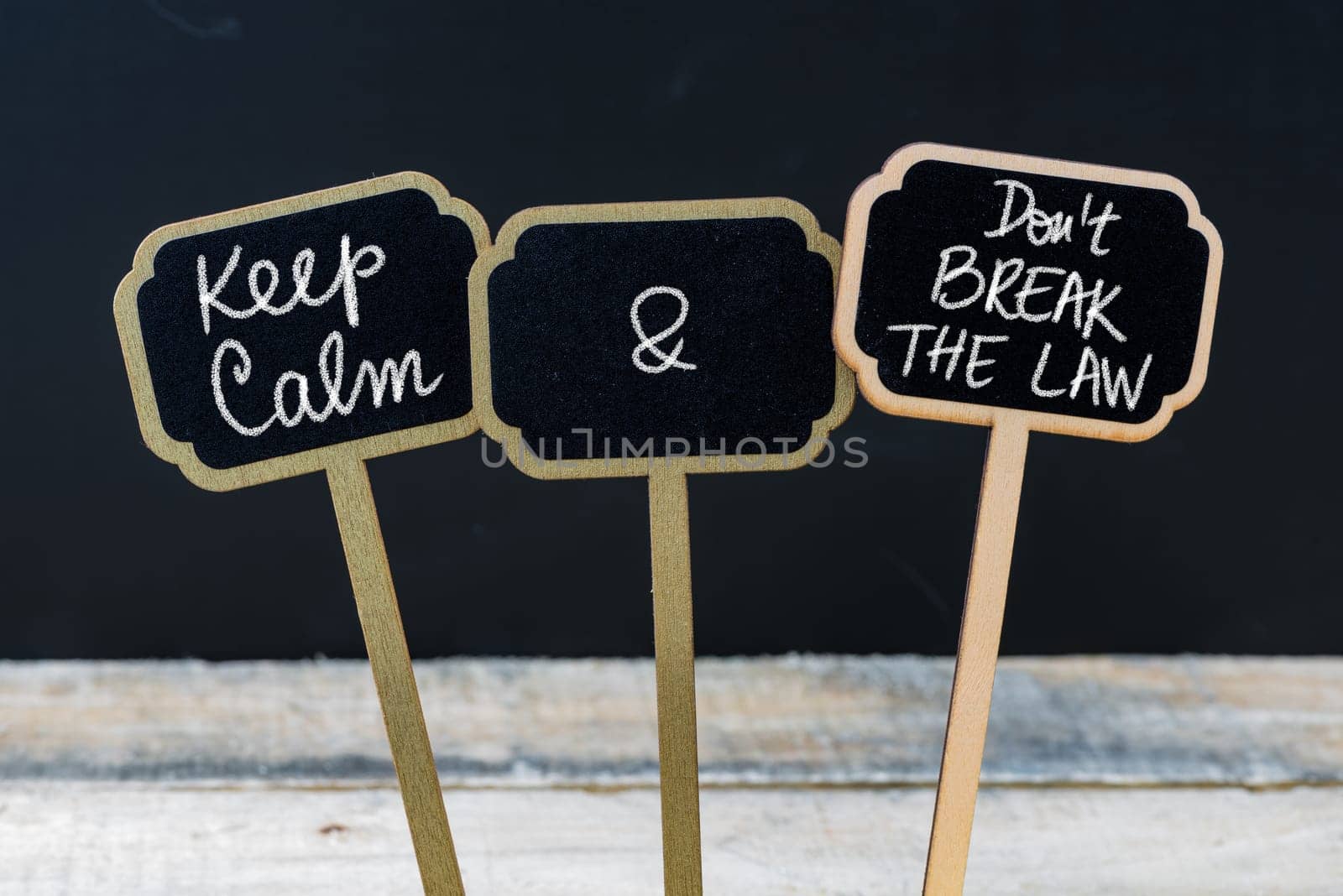 Keep Calm and Do Not Break The Law message written with chalk on mini blackboard labels, defocused chalkboard and wooden table in background. Fun and humor concept