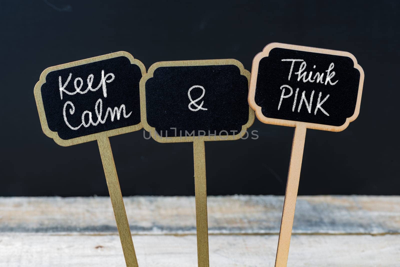 Keep Calm and Think Pink message written with chalk on mini blackboard labels, defocused chalkboard and wooden table in background. Fun and humor concept