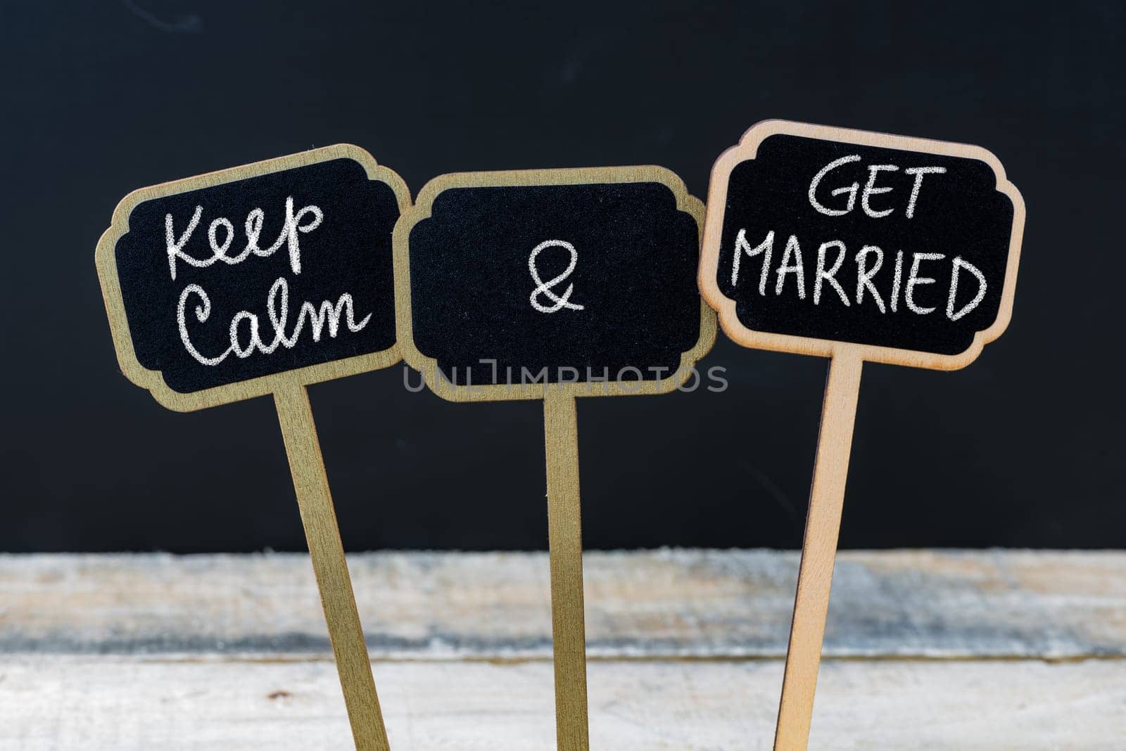 Keep Calm and Get Married message written with chalk on mini blackboard labels, defocused chalkboard and wooden table in background. Fun and humor concept