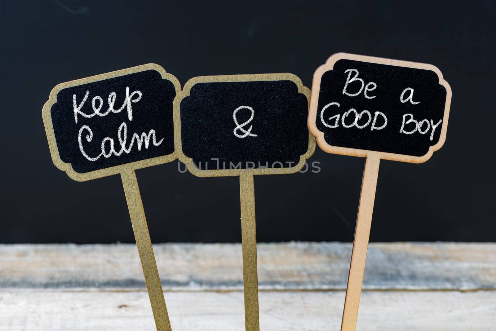 Keep Calm and Be A Good Boy message written with chalk on mini blackboard labels, defocused chalkboard and wooden table in background. Fun and humor concept