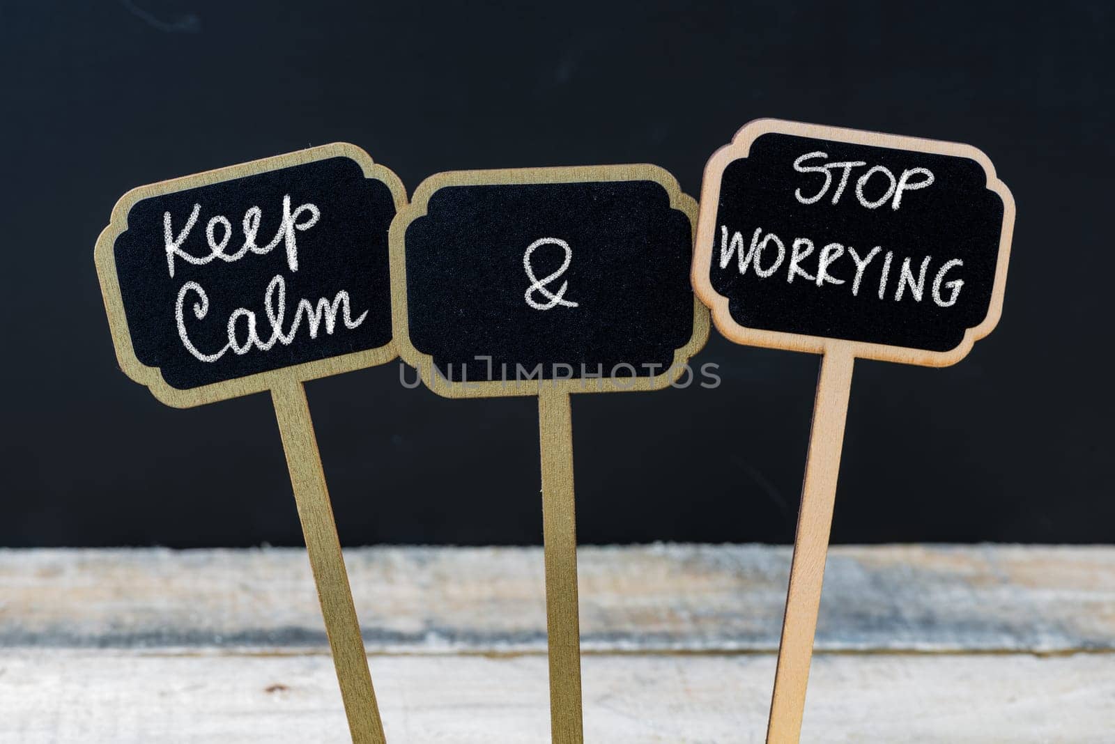 Keep Calm and Stop Worrying message written with chalk on mini blackboard labels, defocused chalkboard and wooden table in background. Fun and humor concept