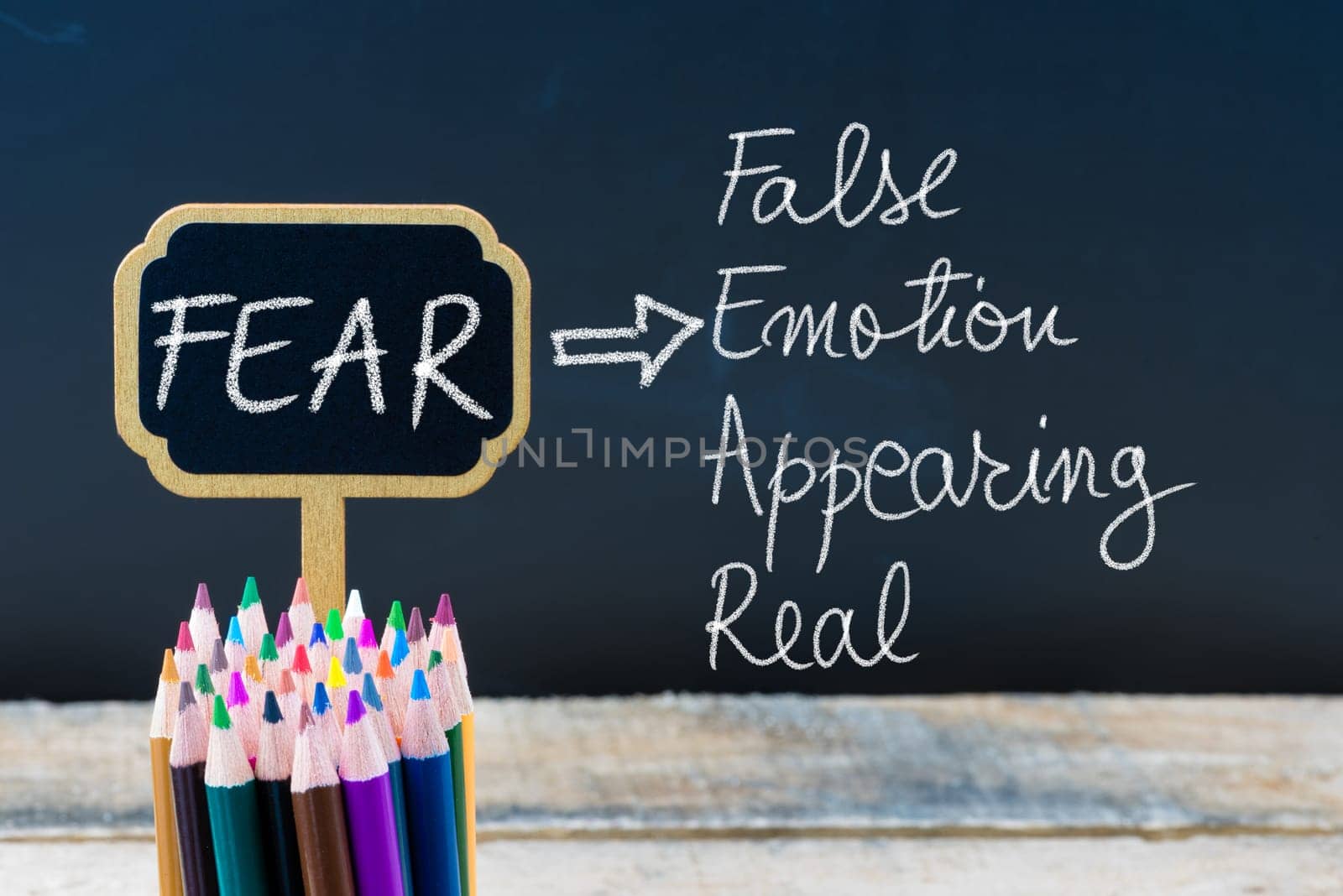 Business Acronym FEAR False Emotion Appearing Real written with chalk on wooden mini blackboard labels and chalkboard background.