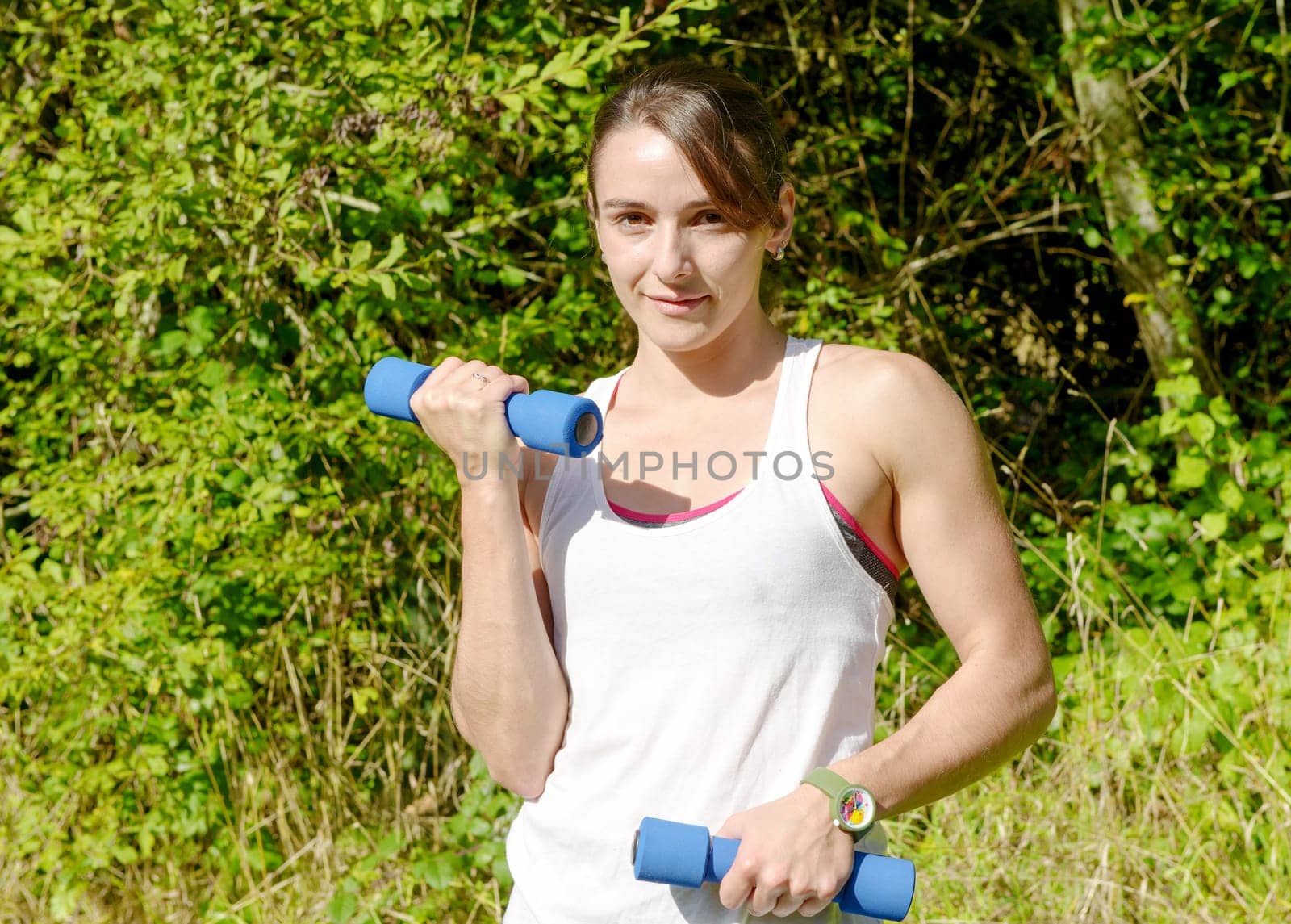Fitness woman doing exercises with blue dumbbells in the countryside