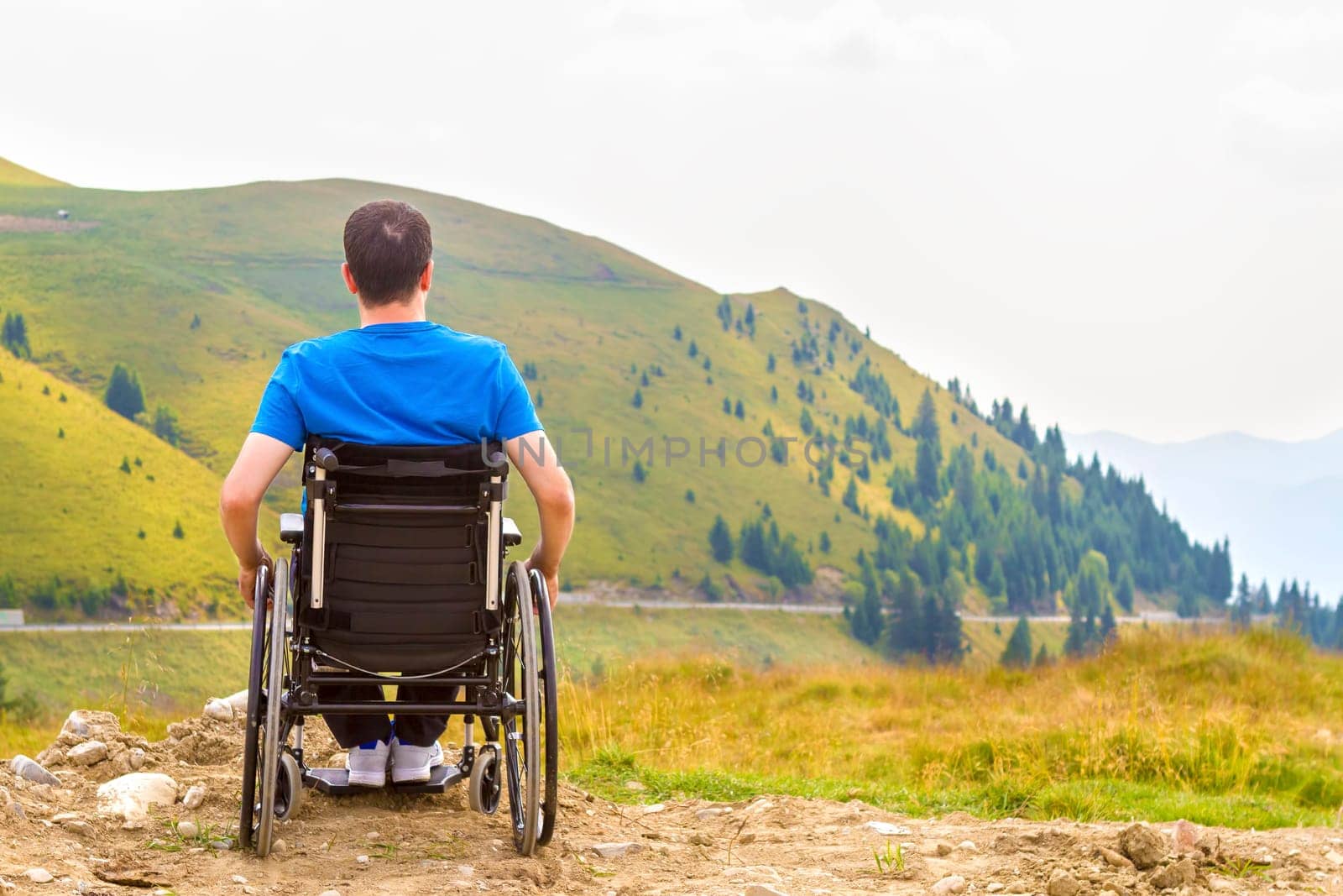 Young man in a wheelchair enjoying fresh air in a sunny day on the mountain.
