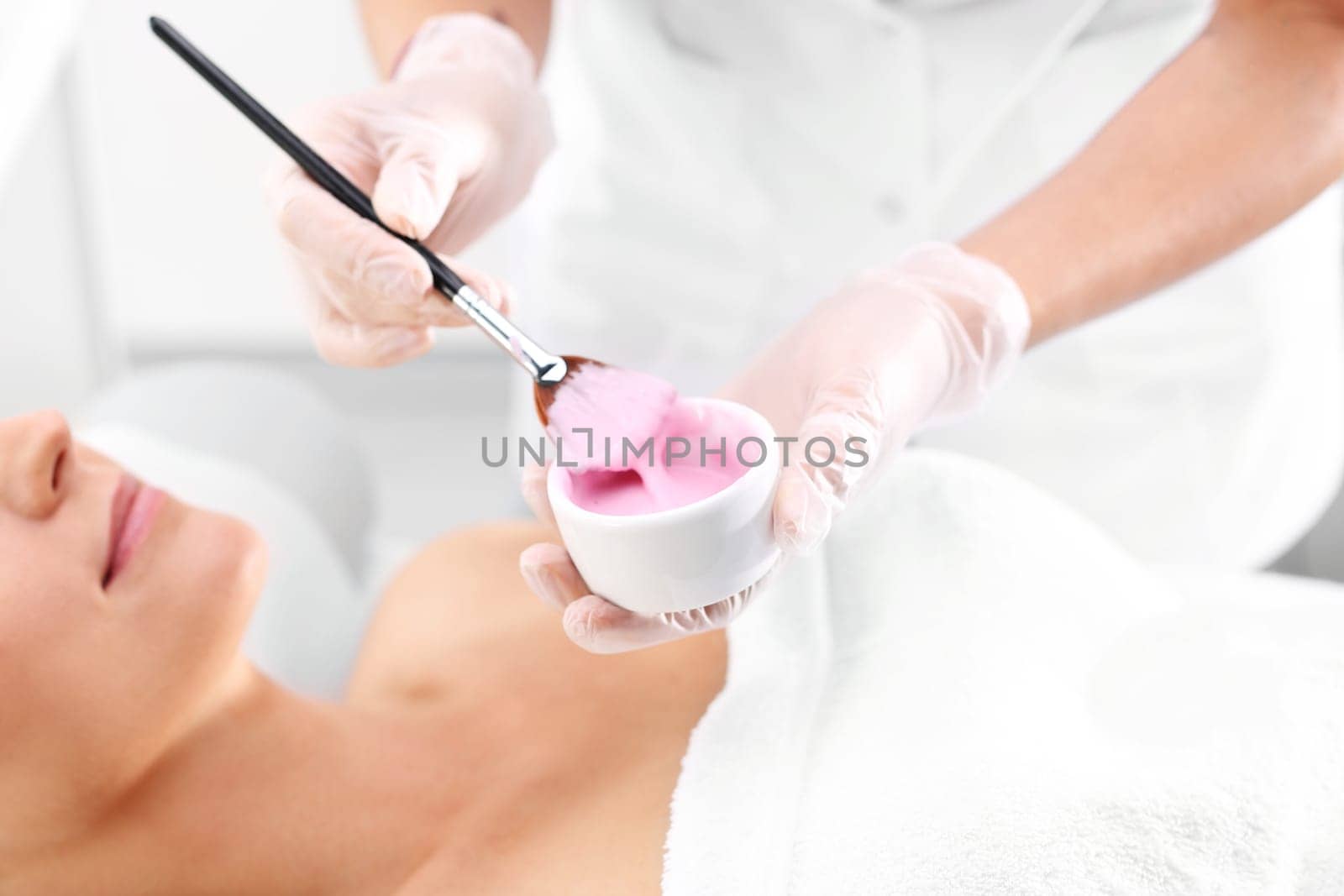 a woman in a beauty salon,a beautician applies a cleavage mask with a brush\n
