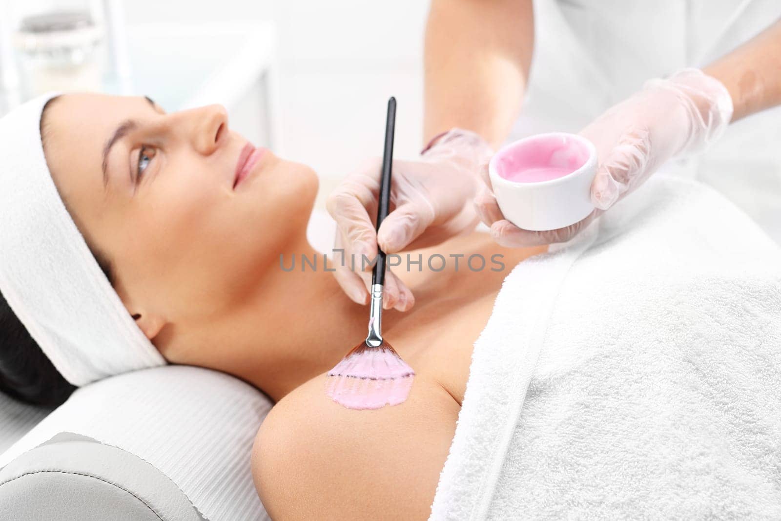 a woman in a beauty salon,a beautician applies a cleavage mask with a brush\n