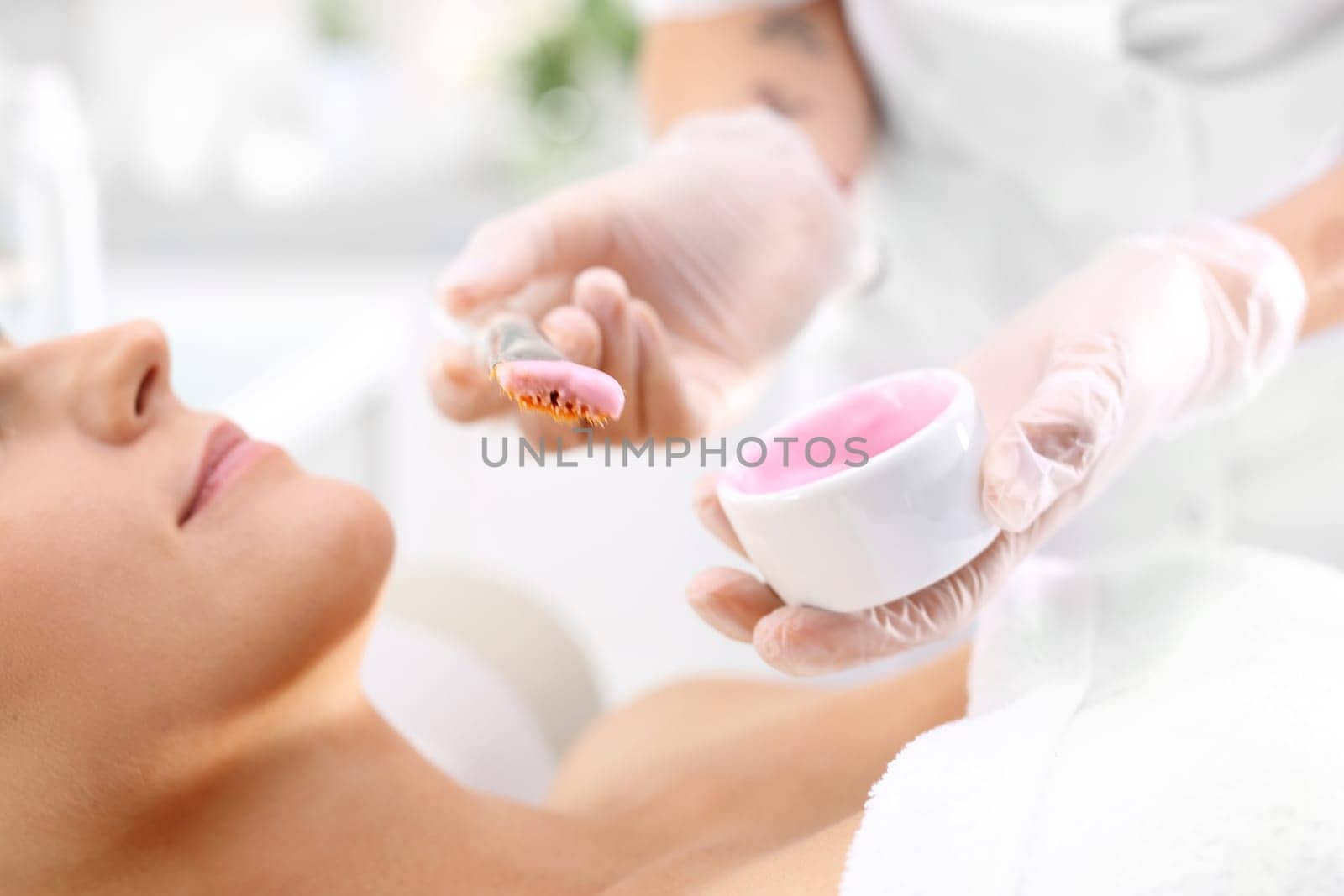 a woman in a beauty salon,a beautician applies a cleavage mask with a brush\n