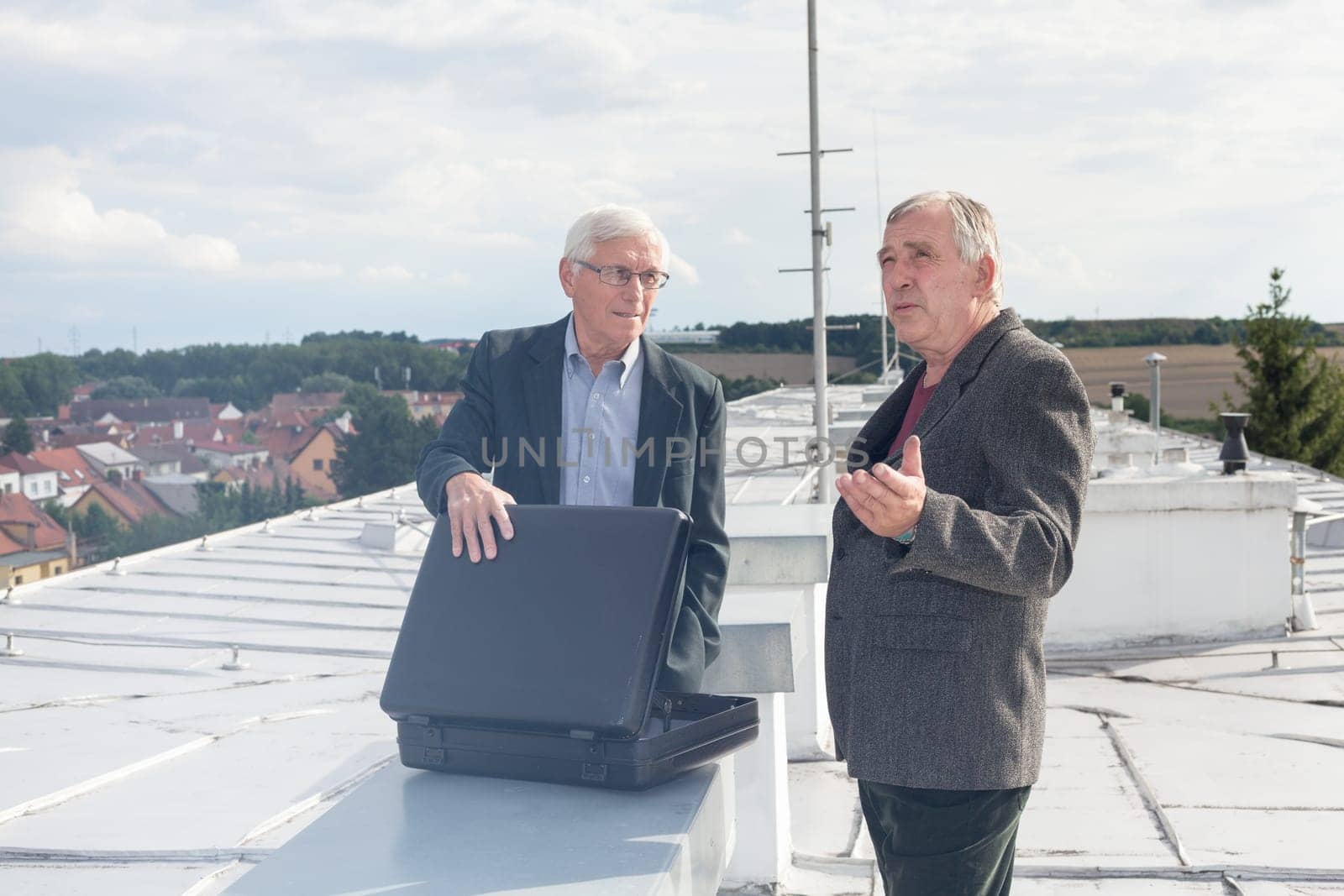 Two senior businessmen with briefcase discussing business deal outdoors on the roof of a building.