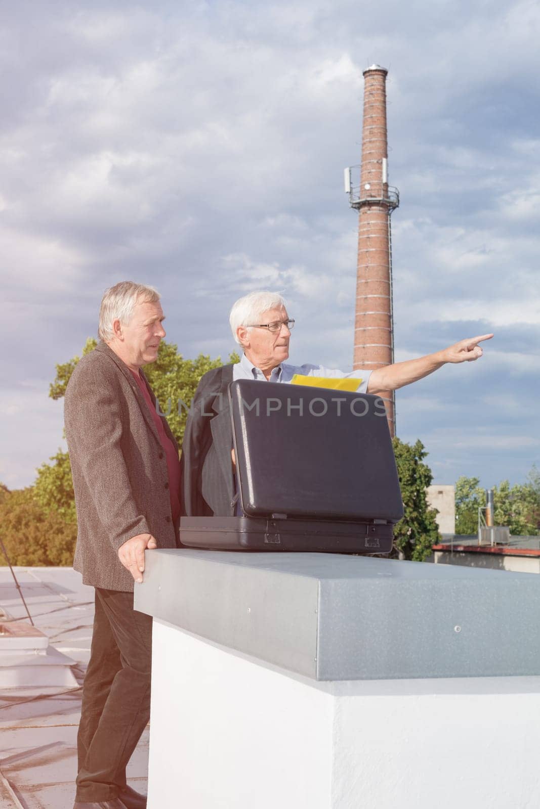 Two senior businessmen with briefcase discussing business outdoors on the roof of a building.