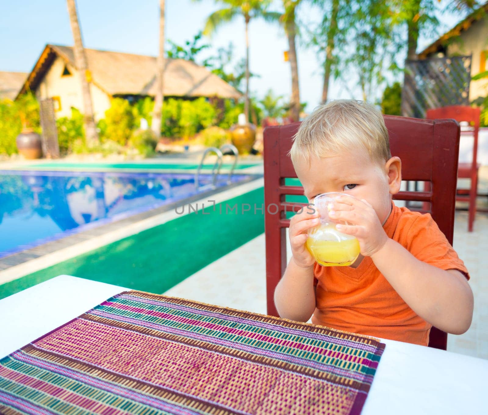 Child drinking juice near a swimming pool